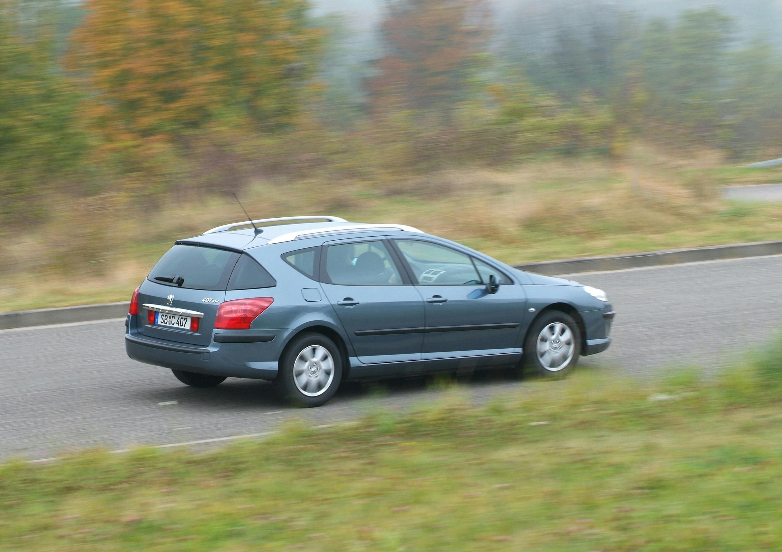 Graues Auto fährt schnell auf einer Landstraße, Hintergrund ist unscharf, Bäume mit Herbstlaub sind teilweise zu sehen.