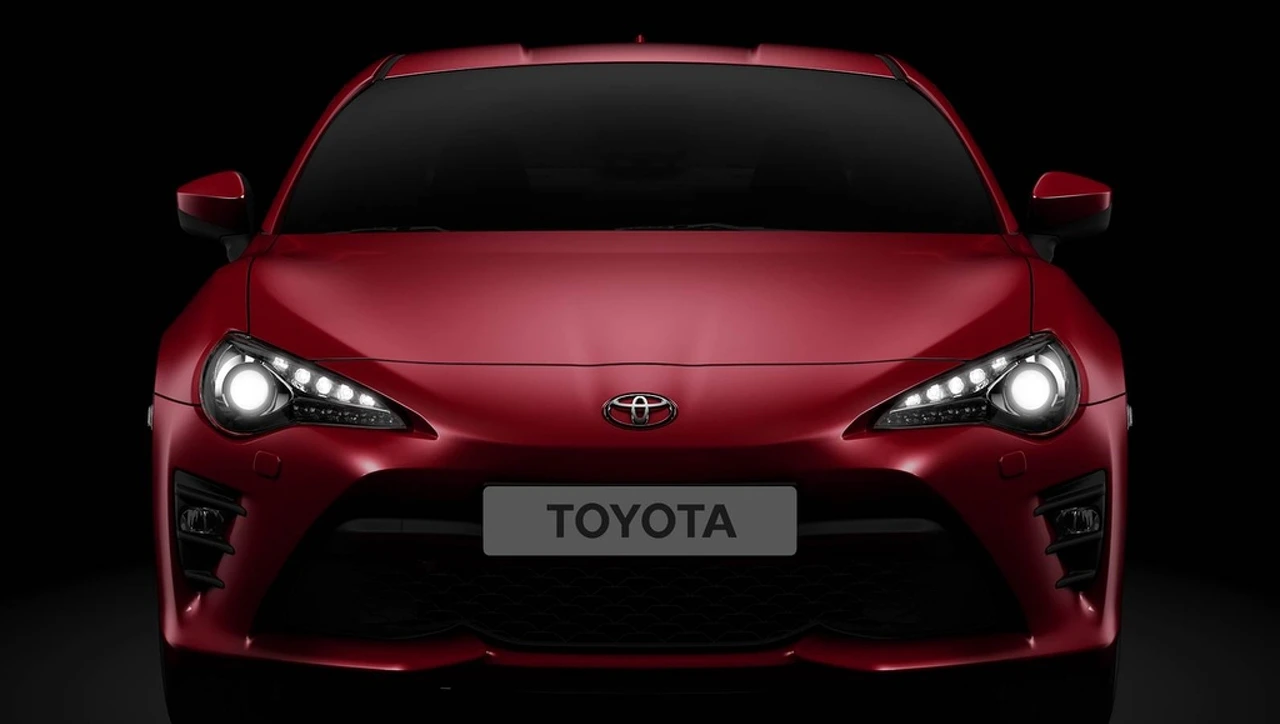 Roter Toyota-Sportwagen in Frontansicht, mit leuchtenden Scheinwerfern, vor dunklem Hintergrund.
