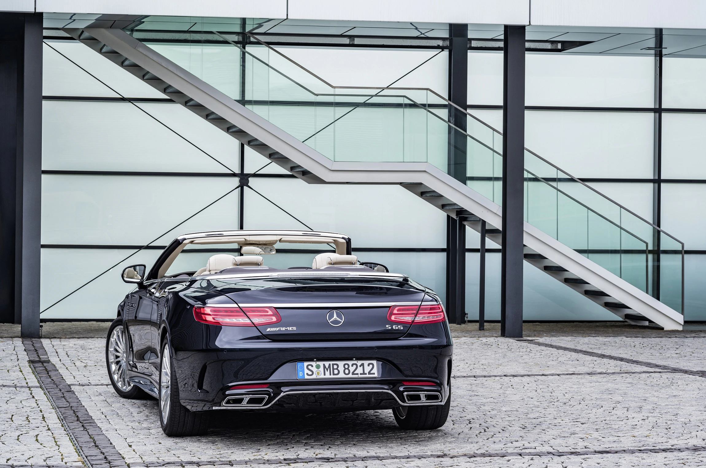 Schwarzes Cabrio Mercedes-AMG S 65 vor moderner Glasfassade und Treppe geparkt.
