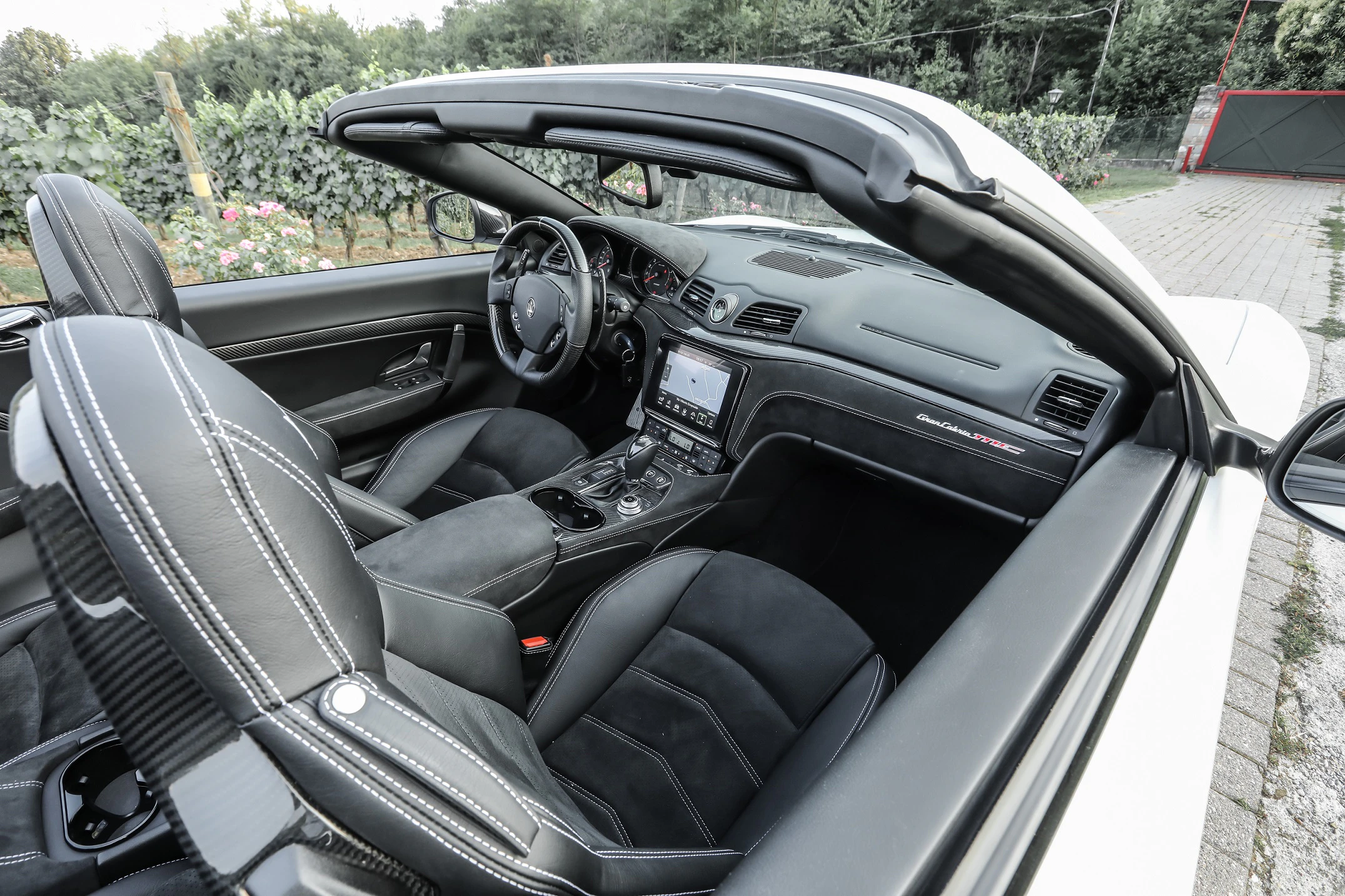 Innenraum eines luxuriösen Cabriolets mit Ledersitzen und modernem Armaturenbrett, geparkt neben einem Weinberg.