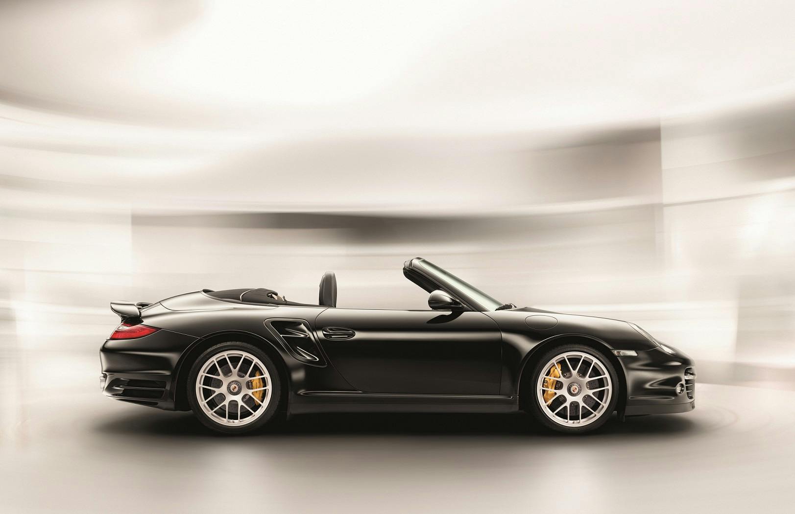 Schwarzer Cabrio-Sportwagen seitlich, unscharfer Hintergrund, silberne Felgen, geöffnetes Verdeck, modernes Design.