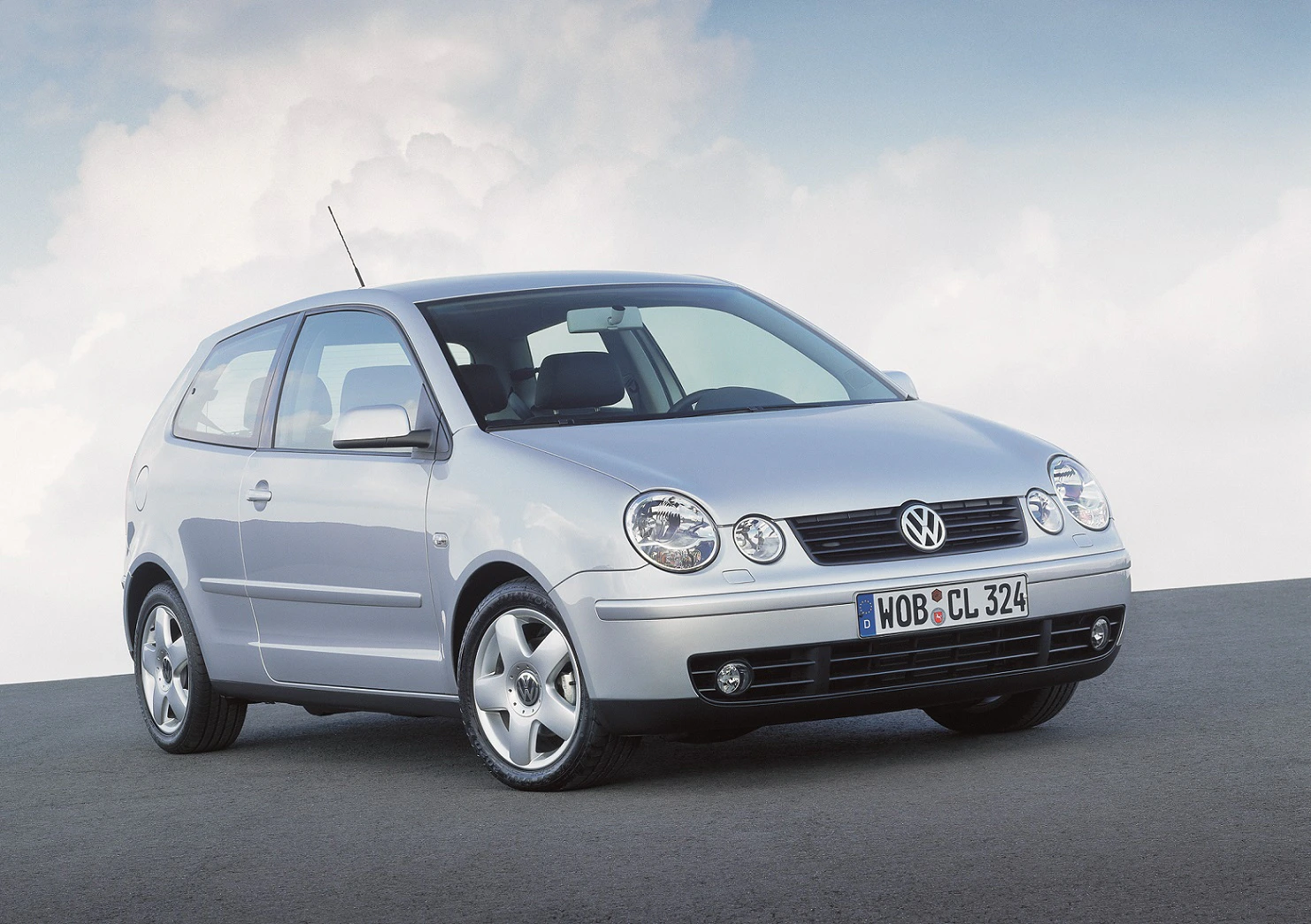 Silberner Volkswagen Polo der dritten Generation, geparkt auf einer asphaltierten Fläche vor bewölktem Himmel.
