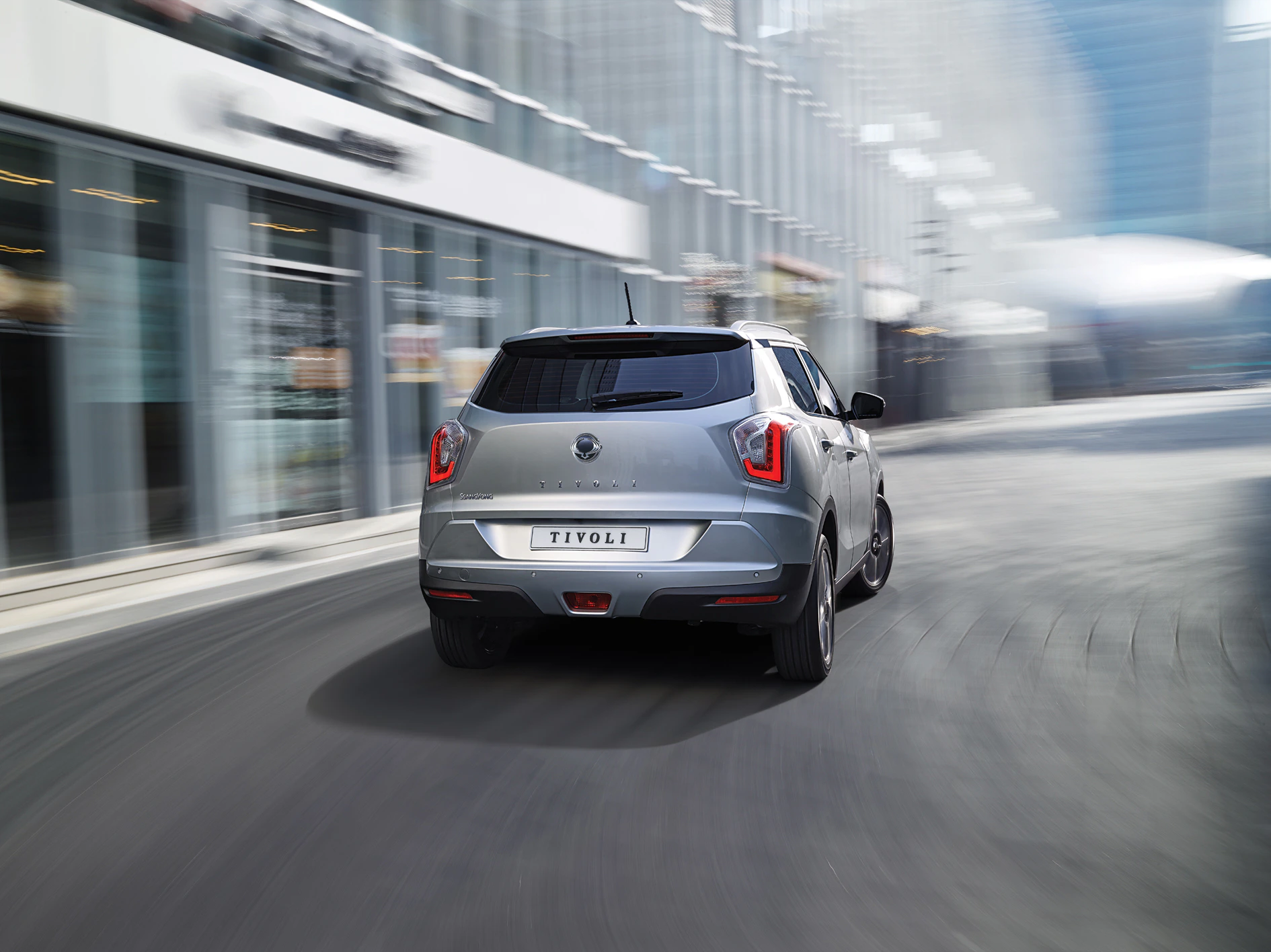 Silberner SUV fährt auf einer modernen, städtischen Straße. Gebäude aus Glas im Hintergrund. Dynamische Bewegung nach vorn.