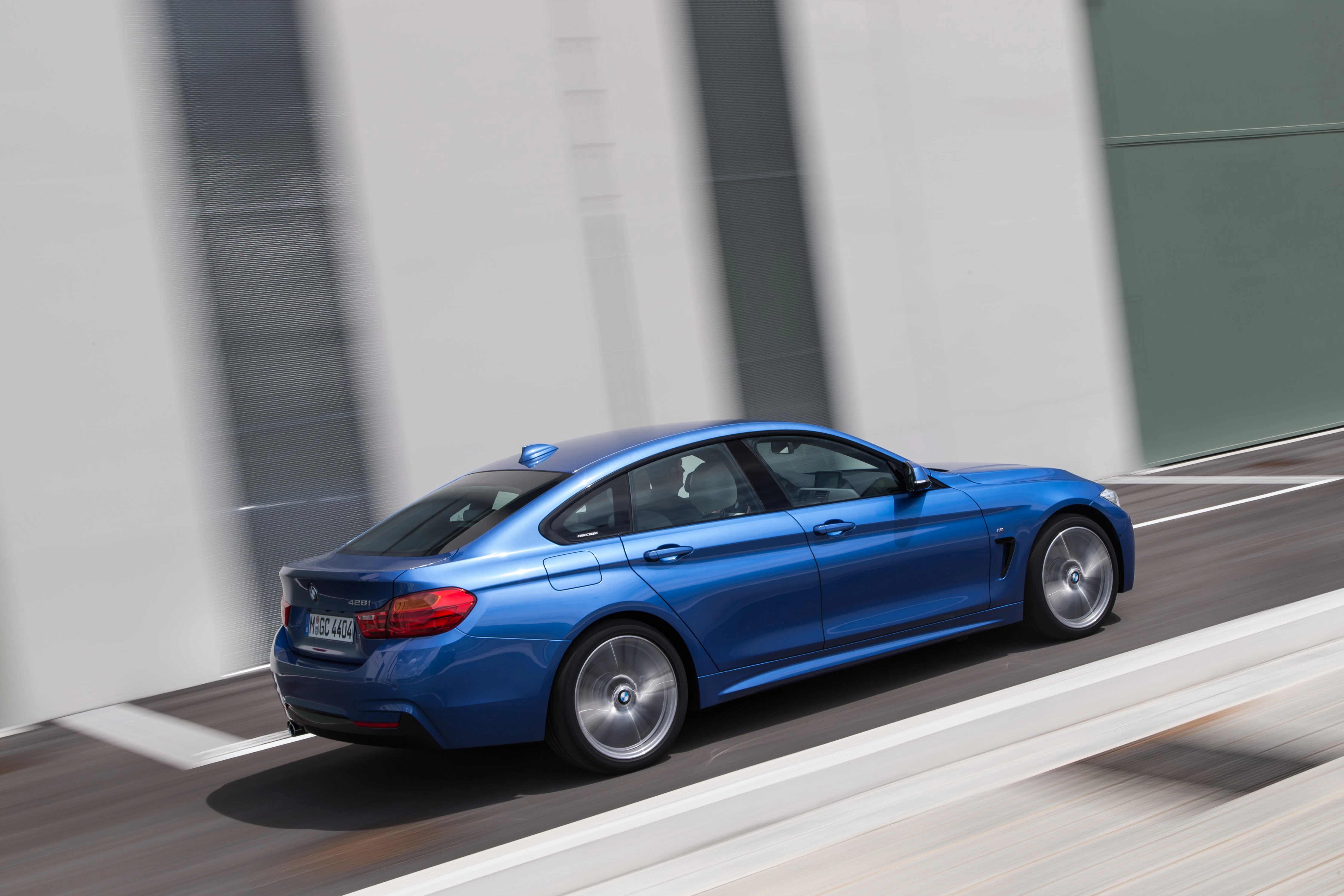 Blaues Auto fährt schnell auf moderner Straße entlang eines Gebäudes. Seitenansicht mit Betonwänden im Hintergrund.