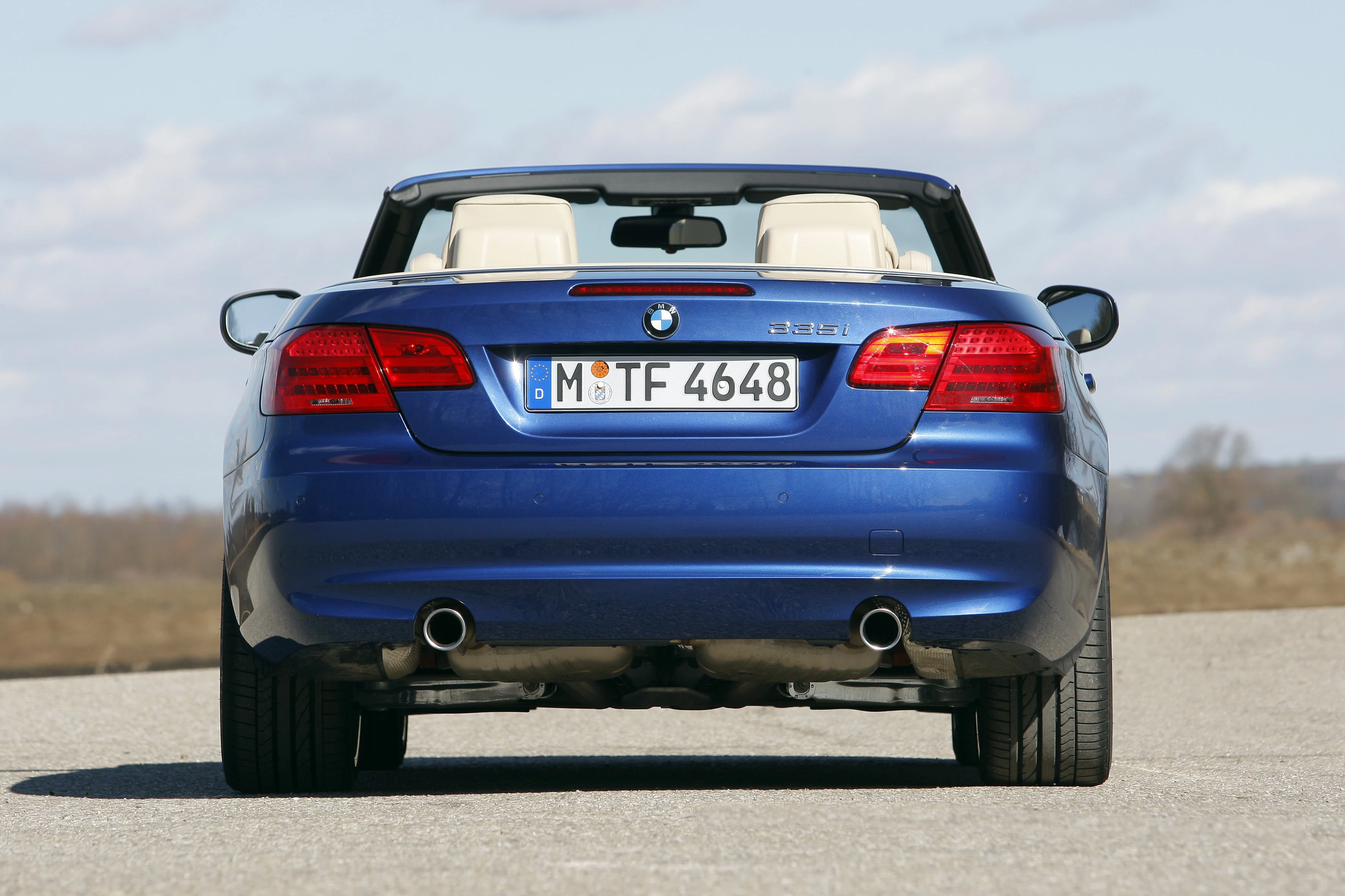 Blaues BMW-Cabrio (E93) von hinten auf einer Straße, mit sichtbarem Kennzeichen, unter klarem Himmel.