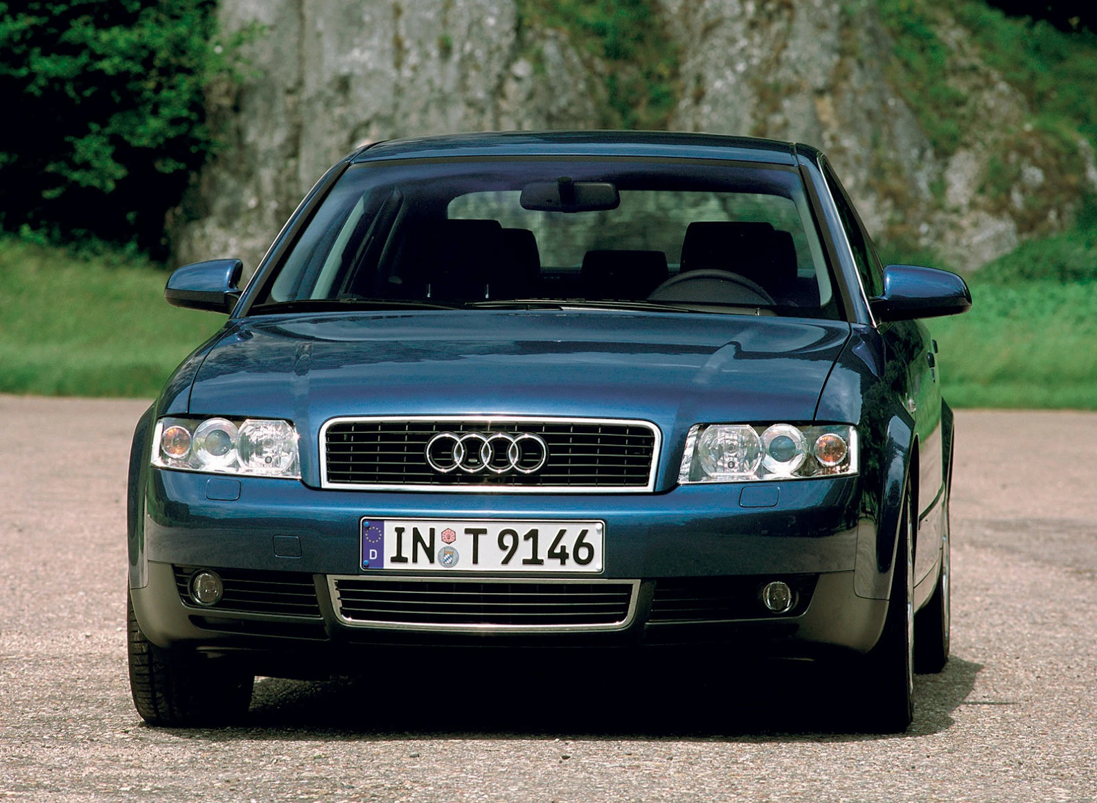 Audi A4, blauer Lack, Frontansicht. Fahrzeug steht auf einem Parkplatz, Bäume und Felsen im Hintergrund.