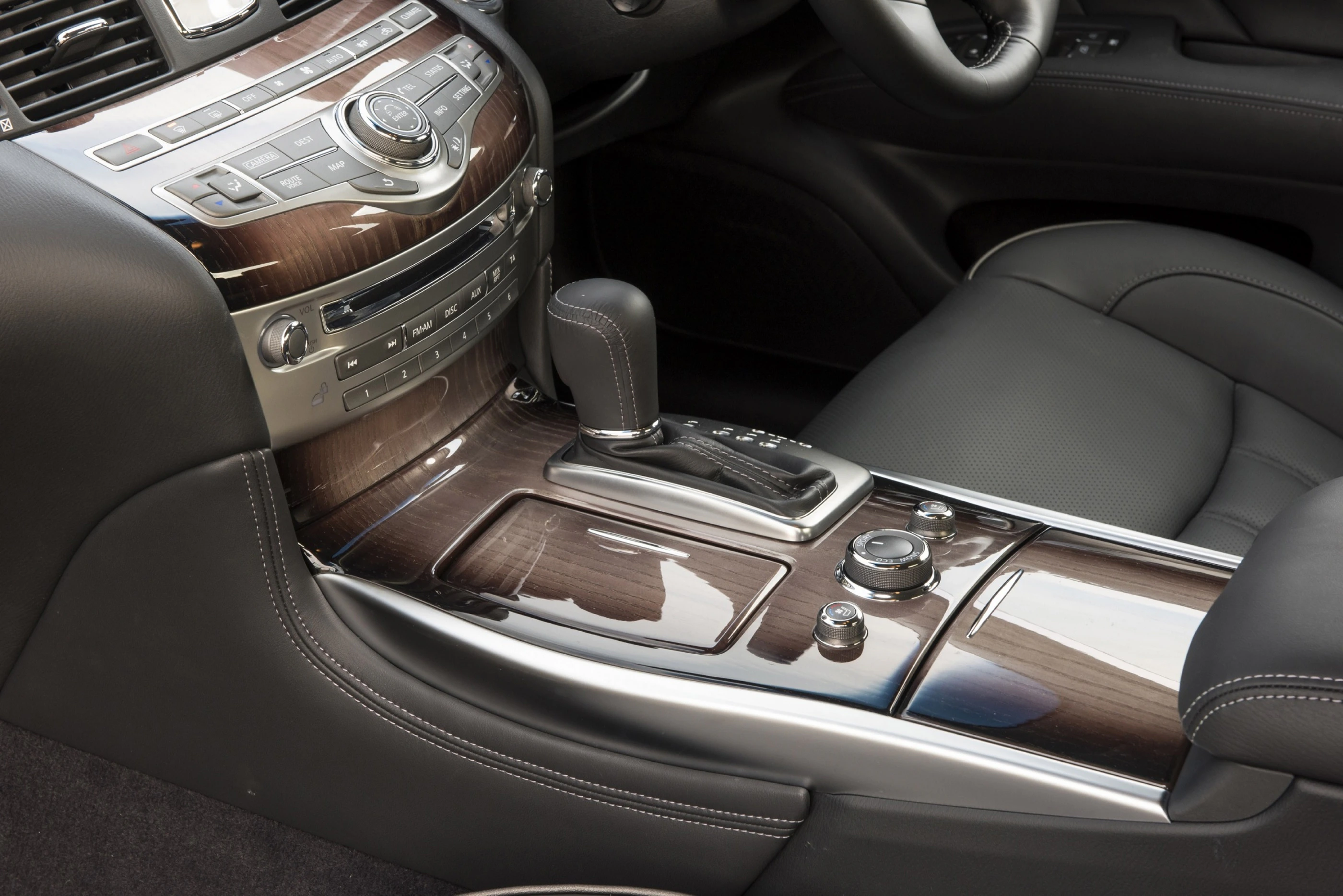 Nahaufnahme eines Autoinnenraums mit eleganter Holzverkleidung, Ledersitzen und einer modernen Mittelkonsole mit Schaltknauf und Bedienelementen.