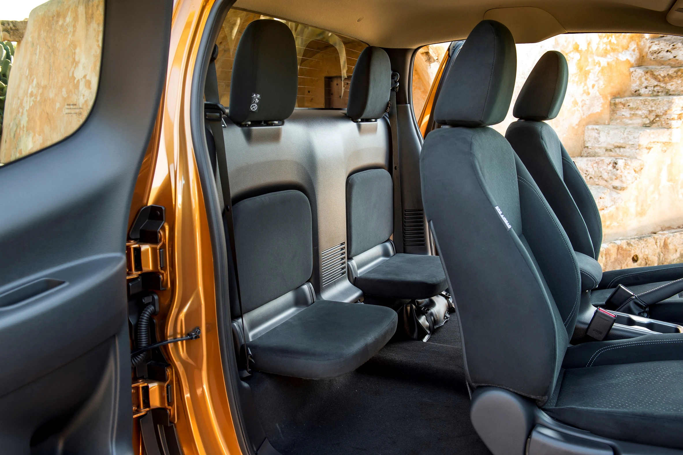 Innenansicht eines orangefarbenen Autos mit hochgeklappten Rücksitzen, schwarzer Polsterung und sichtbarer Mittelkonsole.