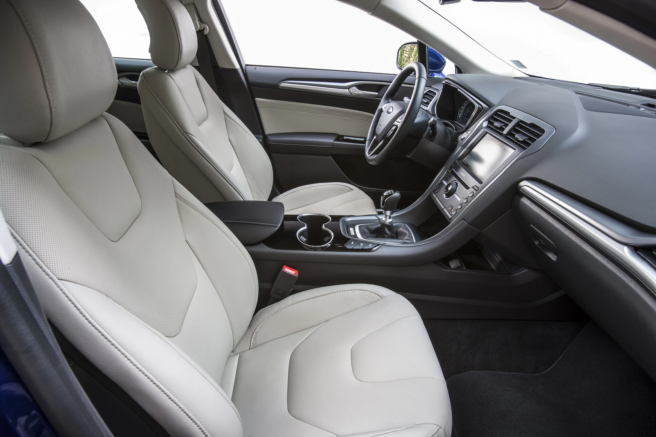 Innenraum eines Autos mit beigen Ledersitzen und modernem Armaturenbrett. Blick auf Mittelkonsole mit Schaltknüppel und Getränkehaltern.
