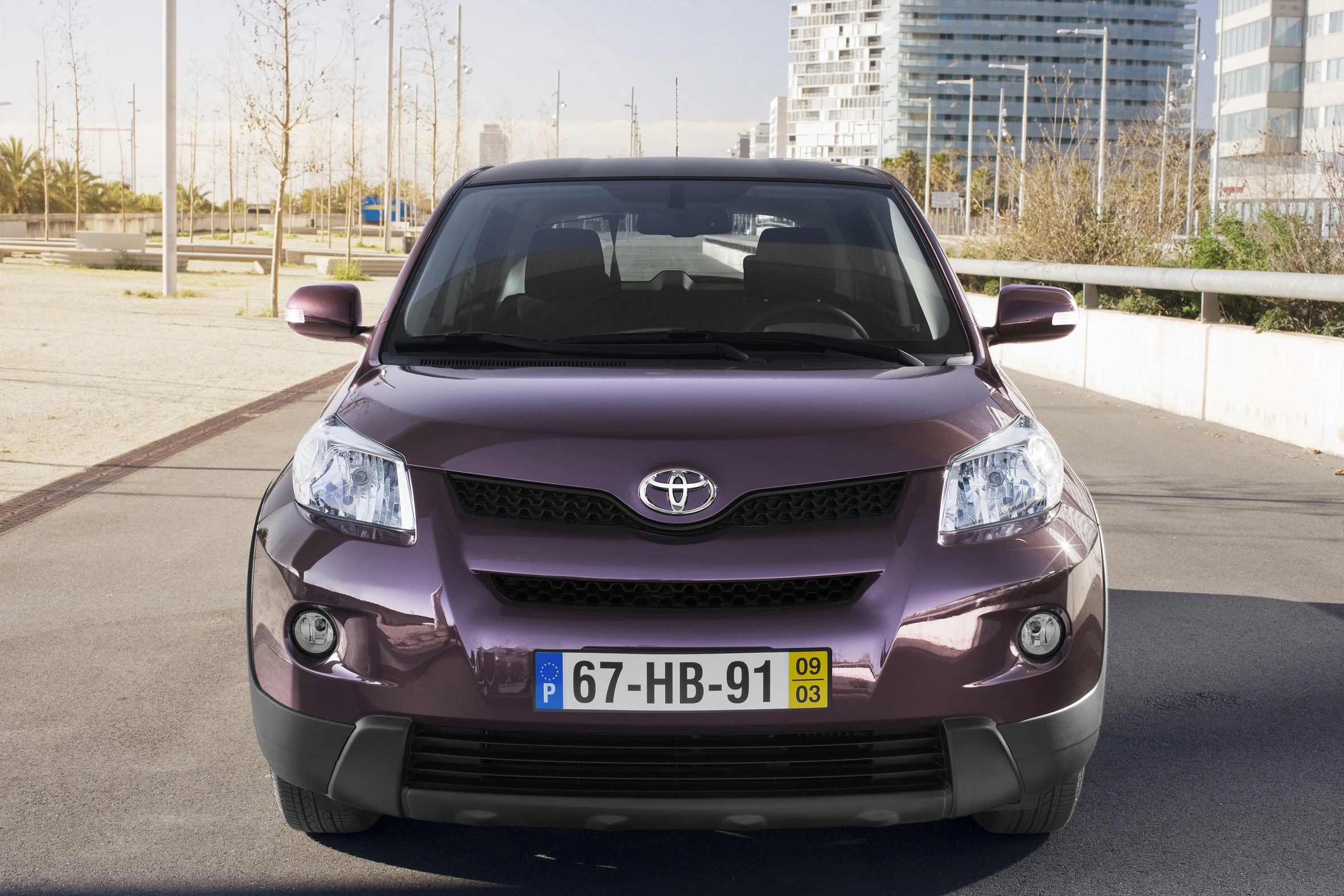Lila Toyota SUV, frontal aufgenommen, auf einem städtischen Parkplatz mit portugiesischem Kennzeichen.