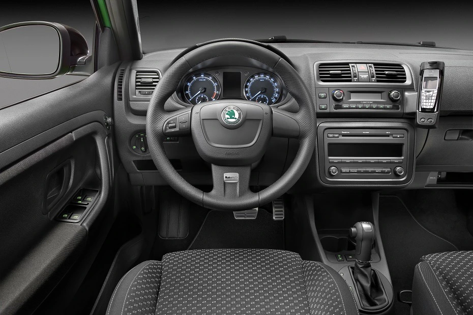 Innenraum eines Autos mit Lenkrad, Armaturenbrett, Tacho und eingebautem Mobiltelefon. Graue Polstersitze und Automatikschaltung.