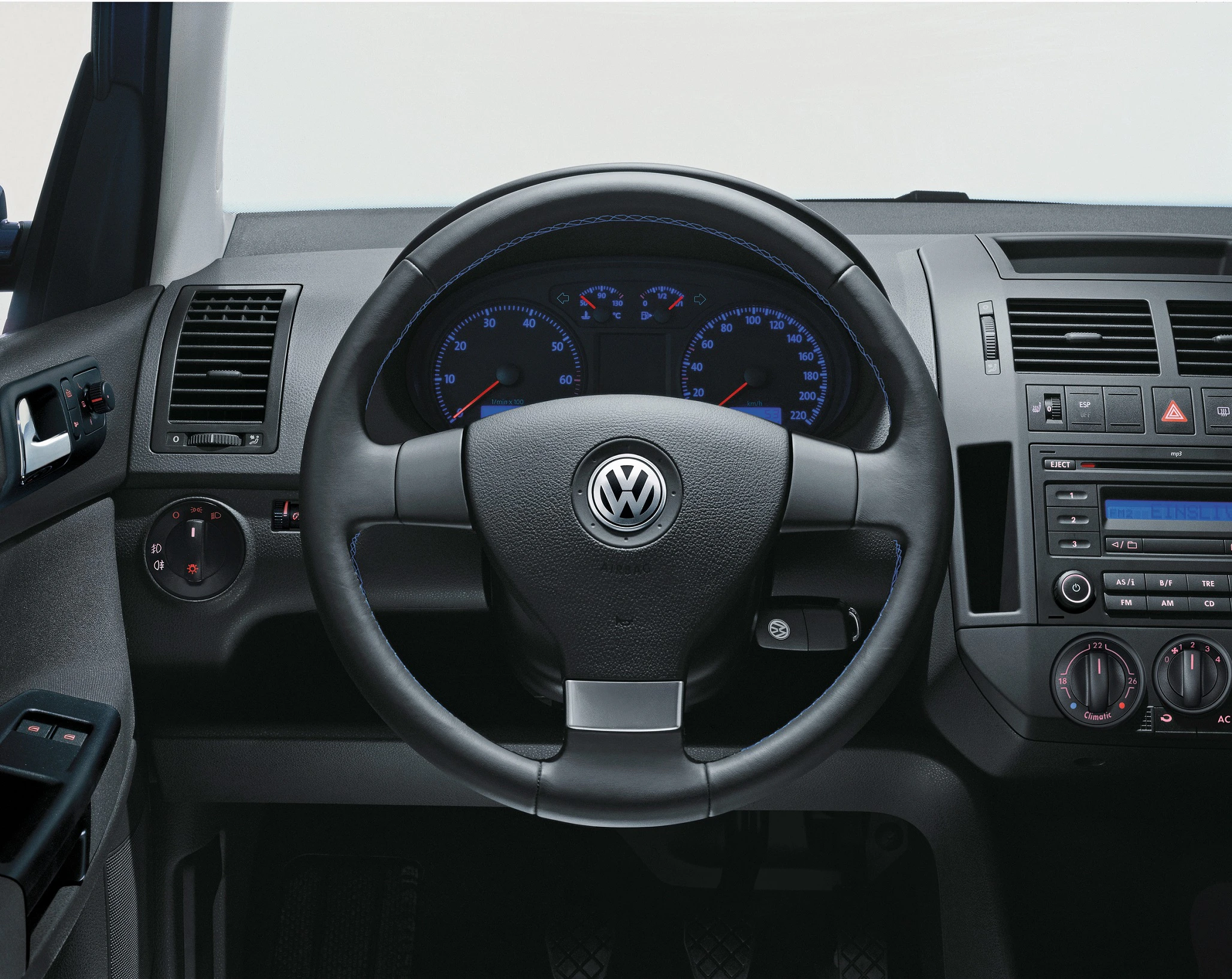 Lenkrad und Armaturenbrett eines Volkswagen-Fahrzeugs mit Tacho und Bedienknöpfen, zentral platziertes VW-Logo.