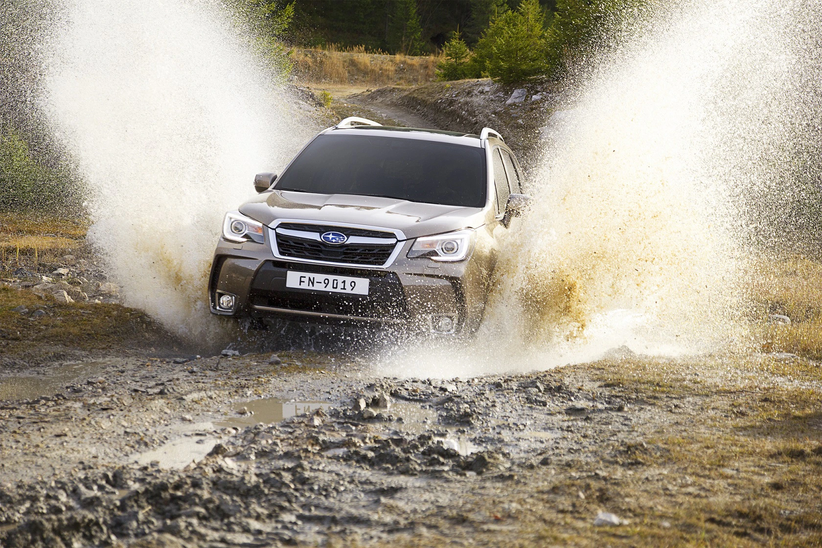 Ein SUV fährt dynamisch durch eine Wasserpfütze auf einer schlammigen Piste, spritzt Wasser in die Luft und zeigt seine Geländetauglichkeit.