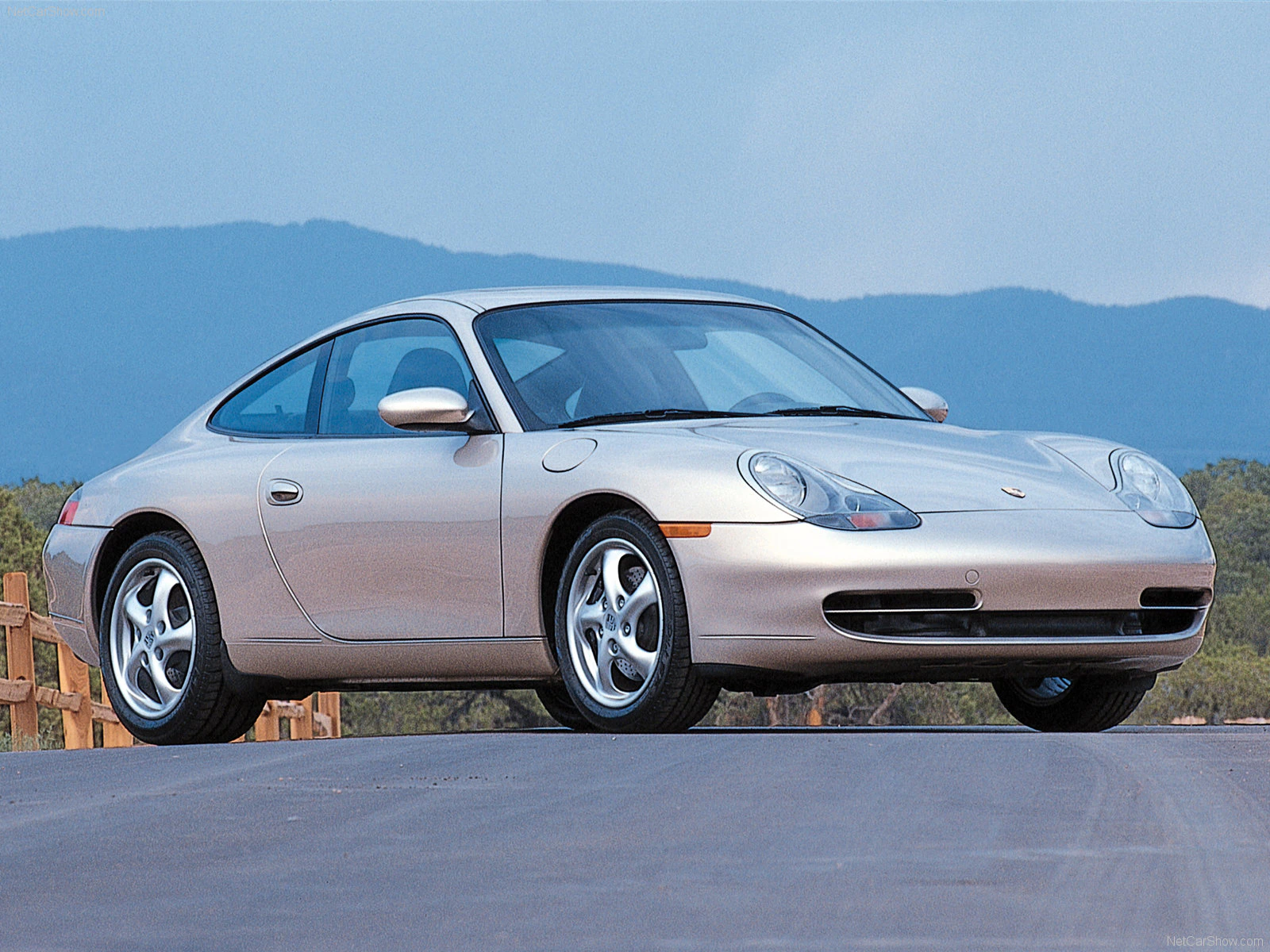Ein silberner Sportwagen (Porsche 911) steht auf einer Straße vor einer Bergkulisse unter klarem Himmel.