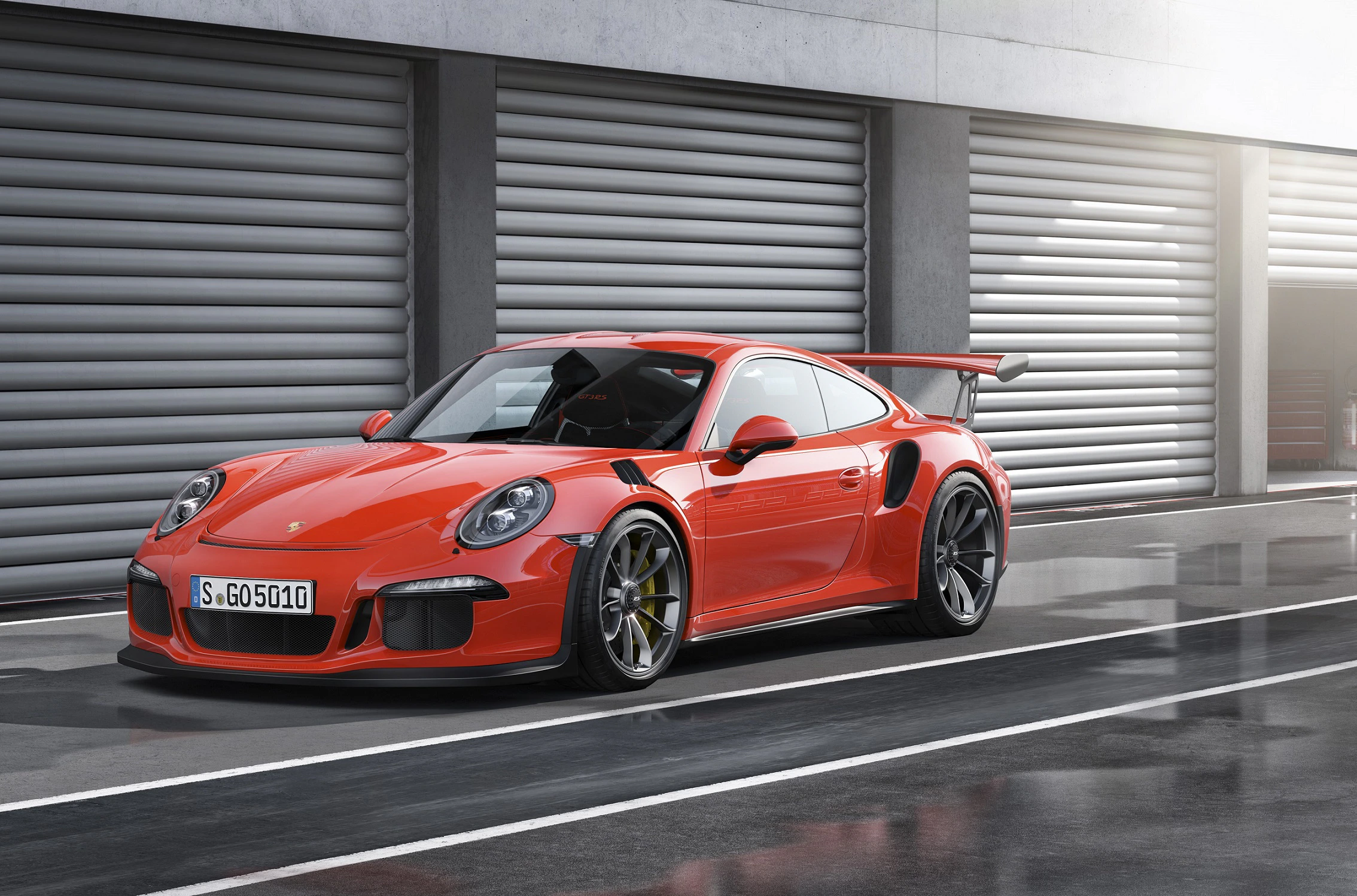 Ein roter Sportwagen parkt vor grauen Garagentoren. Der Wagen hat breite Reifen, einen Heckspoiler und aggressive Karosseriedetails.
