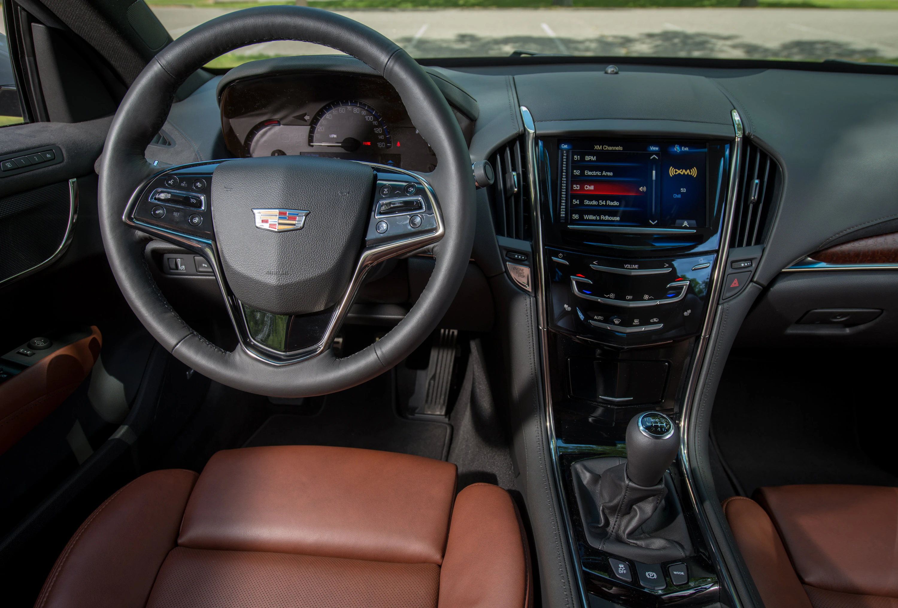Innenraum eines Autos mit braunen Sitzen, Lenkrad, digitalem Display und Schalthebel. Moderne Bedienelemente und dunkle Verkleidung.