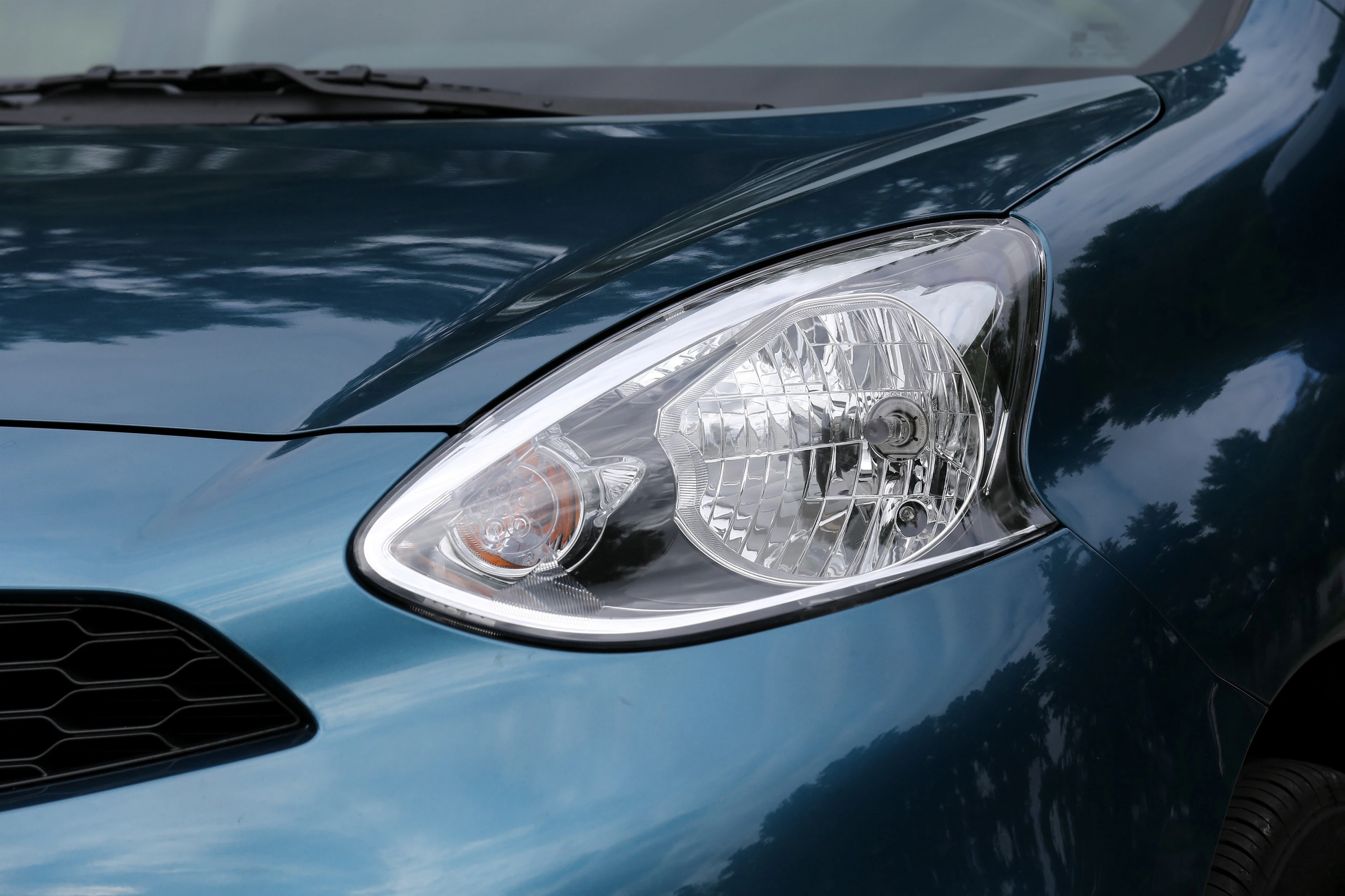 Nahaufnahme eines blauen Autos mit detailreichem Scheinwerfer und glänzender Karosserie.