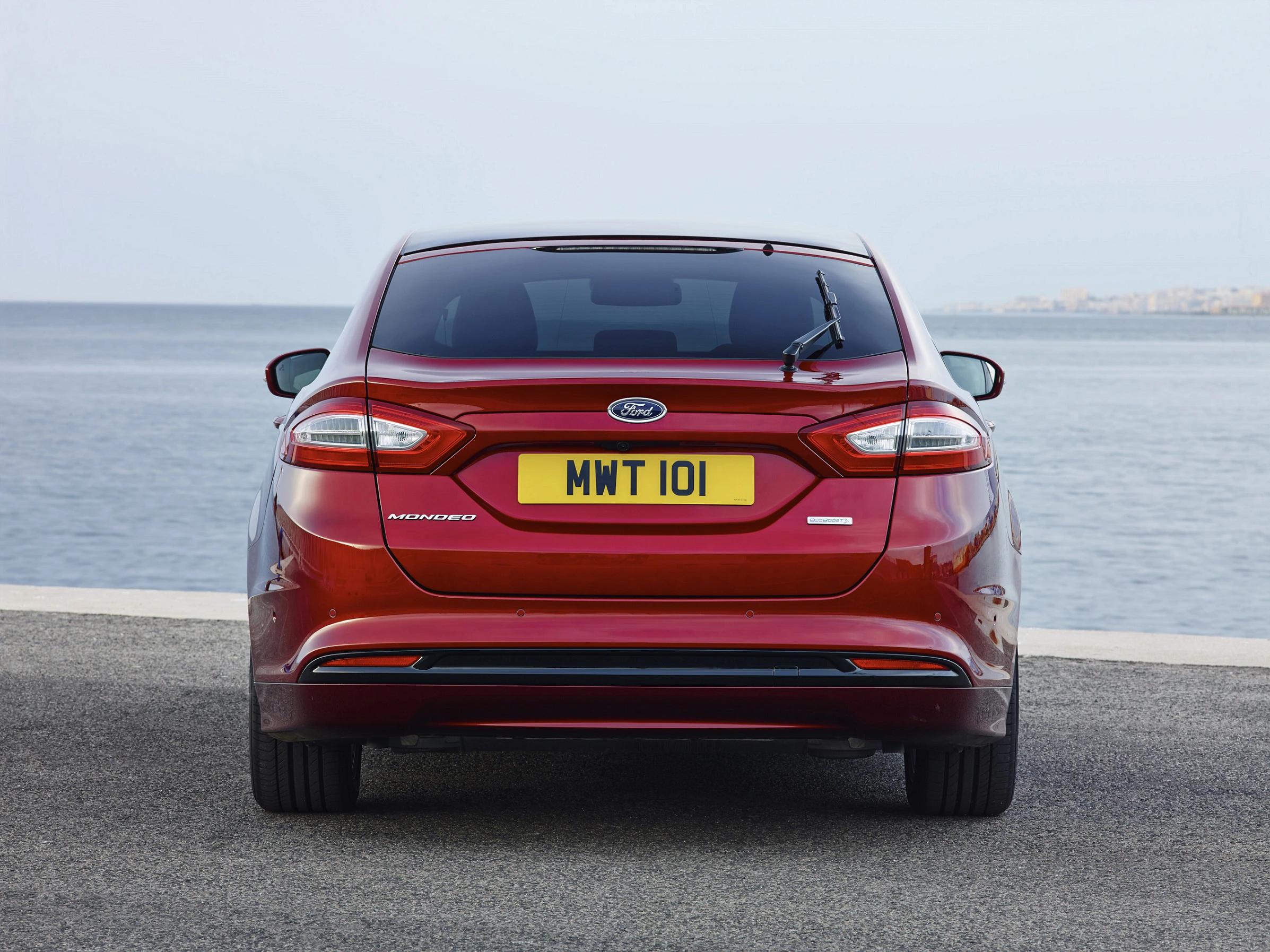 Roter Ford Mondeo Hybrid von hinten, steht vor einem ozeanischen Hintergrund, mit dem Kennzeichen "MWT 101".