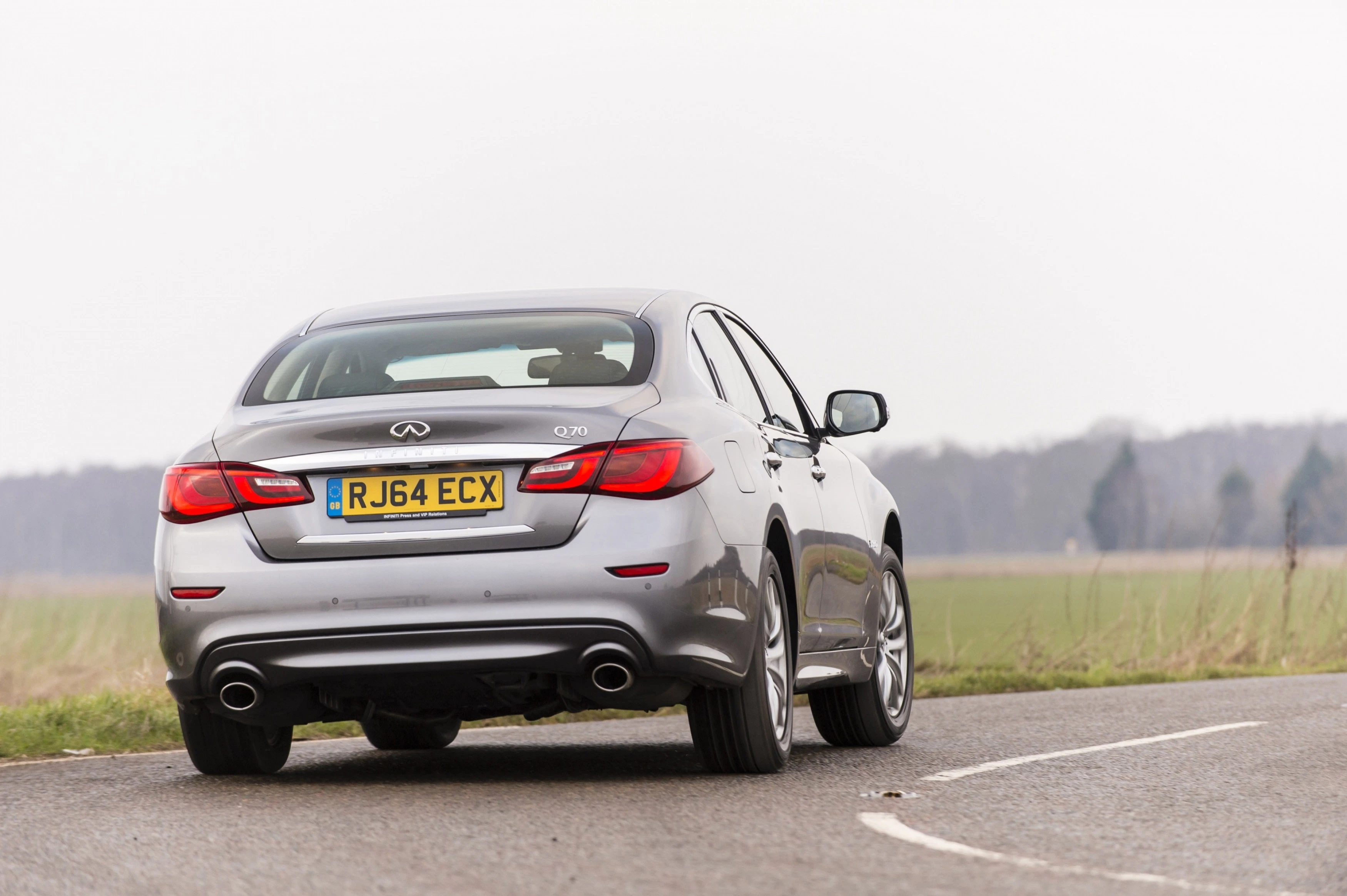 Silberner Infiniti Q70 auf einer Landstraße, Rückansicht, britisches Nummernschild, mit Bäumen im Hintergrund.