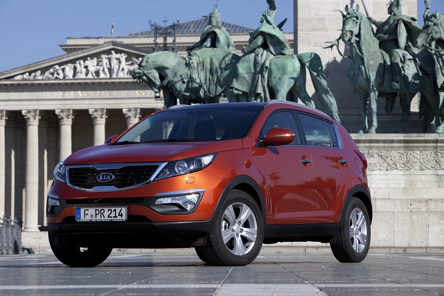 Roter SUV Kia Sportage vor einem historischen Gebäude mit Statuen von Pferden und Reitern im Hintergrund.