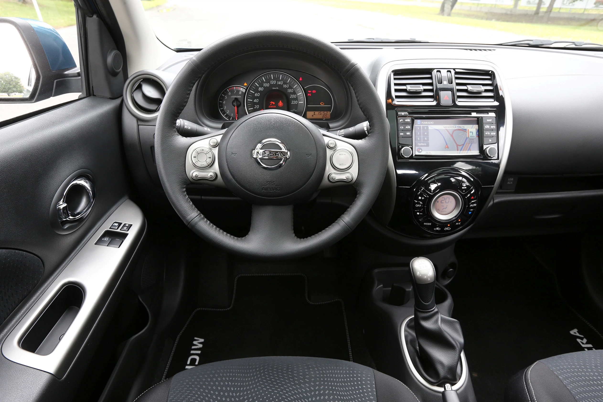 Innenansicht eines Autos mit Lenkrad, Tachometer, Bildschirm mit Navigationssystem und Schalthebel. Modernes, kompaktes Design.