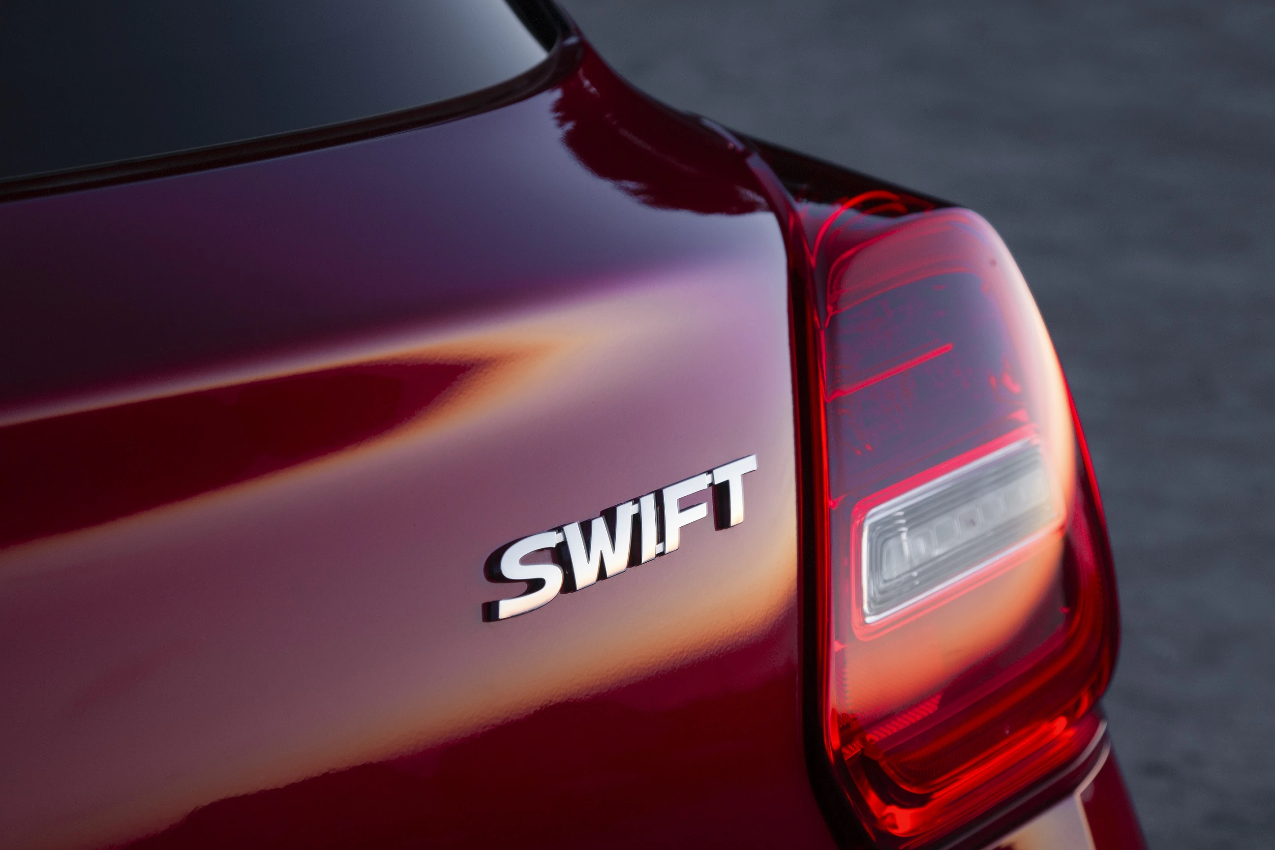 Nahaufnahme eines roten Autos mit dem Schriftzug „SWIFT“ auf dem Heck und einer leuchtenden Rückleuchte.