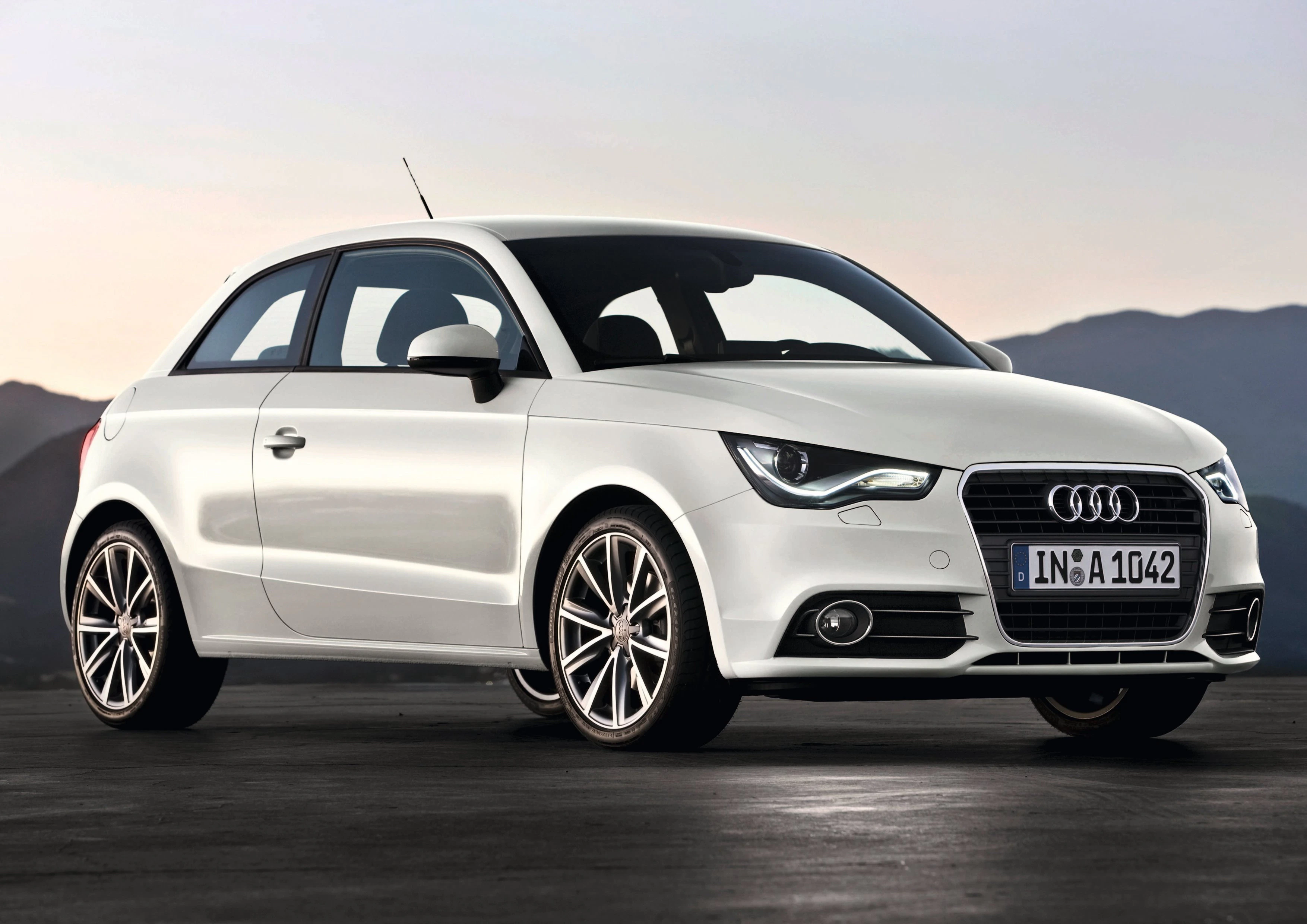 Weißer Audi A1 auf einer Straße vor einem Hintergrund mit blauen Bergen und Himmel bei Sonnenuntergang.
