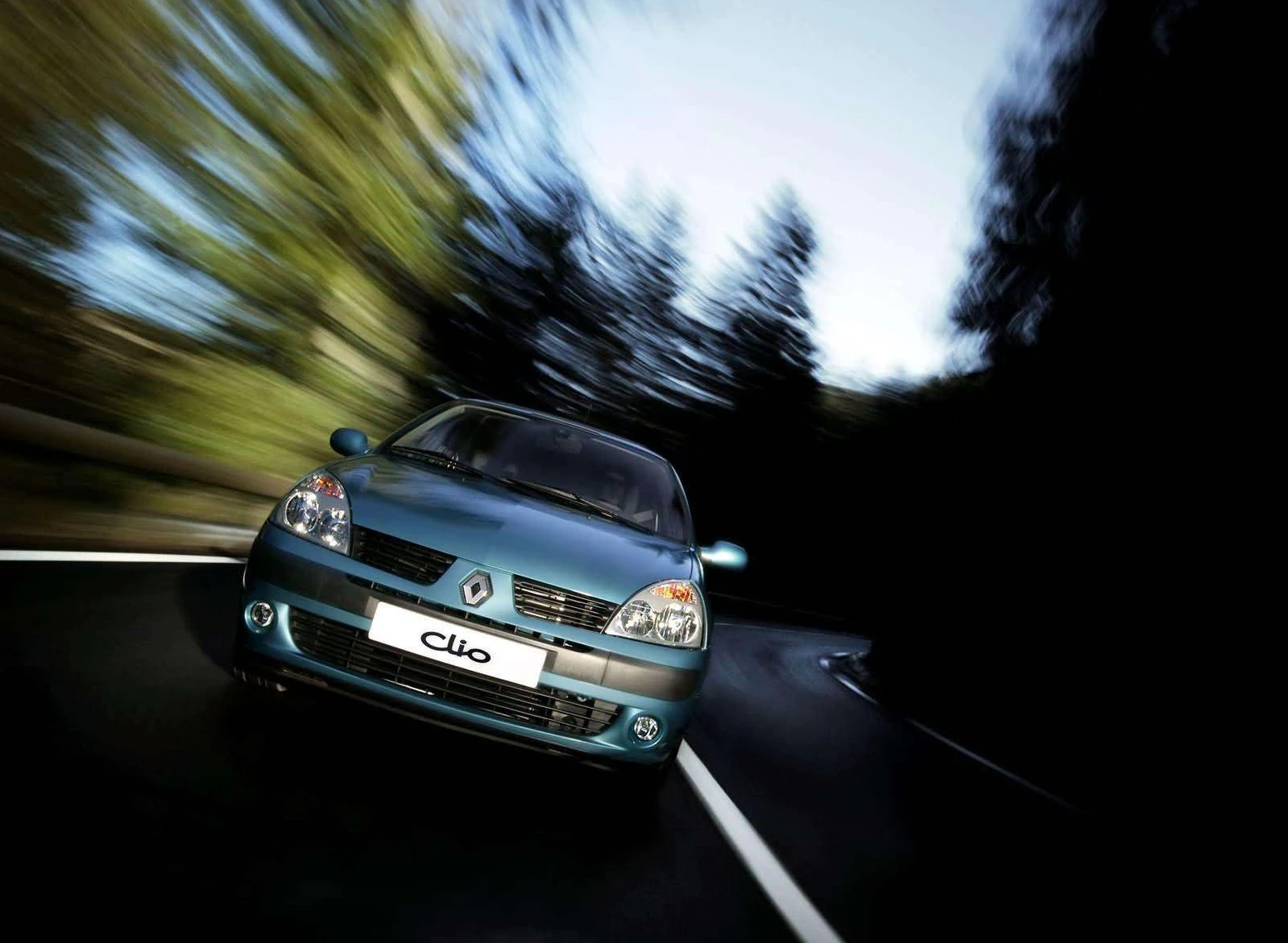 Renault Clio fährt dynamisch durch kurvenreiche, bewaldete Straße mit leichtem Motion Blur, repräsentiert Geschwindigkeit und Agilität.