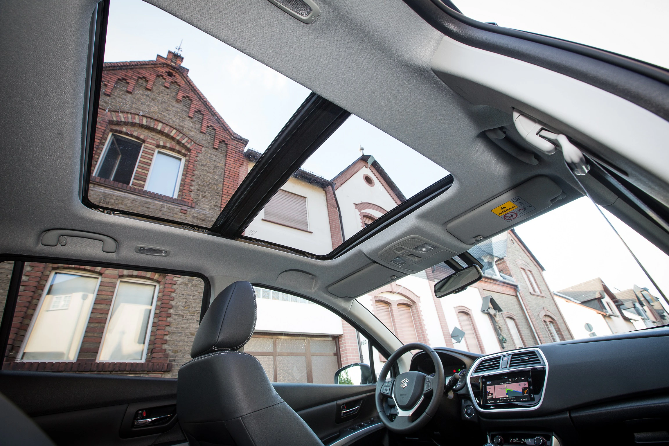 Blick aus dem Innenraum eines Autos mit Panoramadach auf historische Ziegelgebäude.