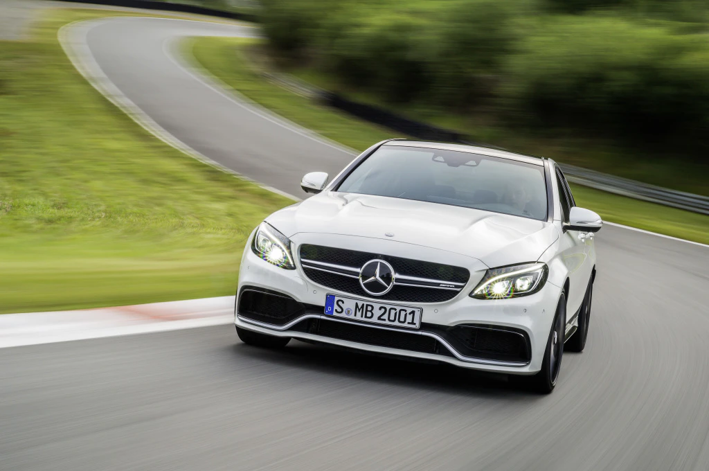 Ein weißer Mercedes fährt schnell auf einer kurvigen, asphaltierten Rennstrecke mit grüner Umgebung.
