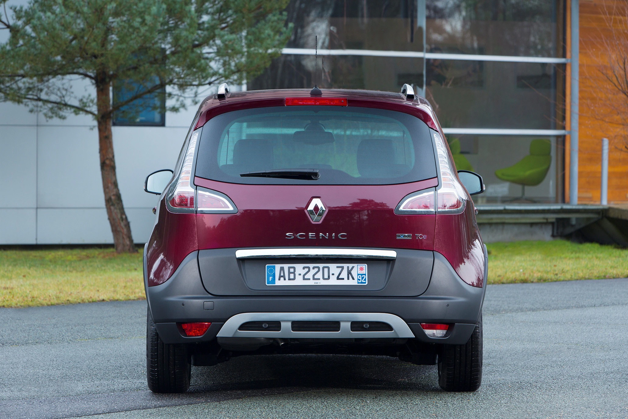 Roter Renault Scenic auf Parkplatz, Heckansicht. Gebäude und Baum im Hintergrund. Französisches Kennzeichen sichtbar.