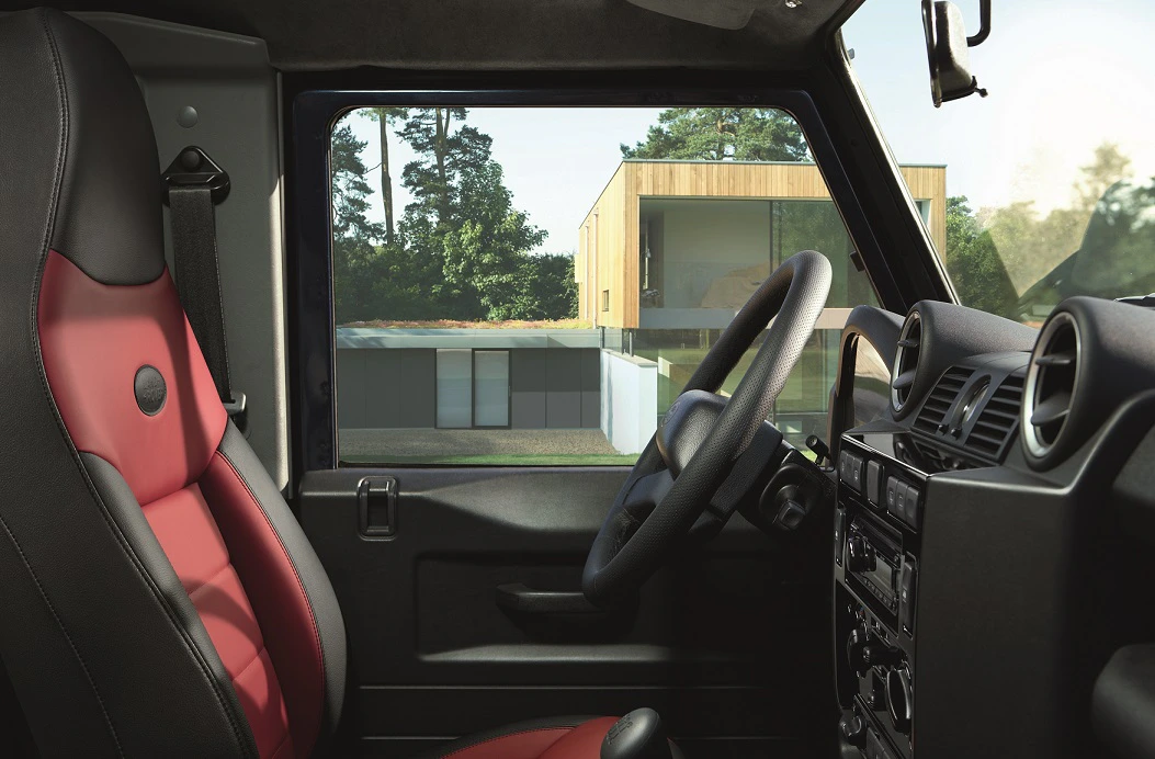 Innenraum eines Autos mit rot-schwarzem Sitz, Blick nach draußen auf ein modernes Gebäude und Bäume im Hintergrund.