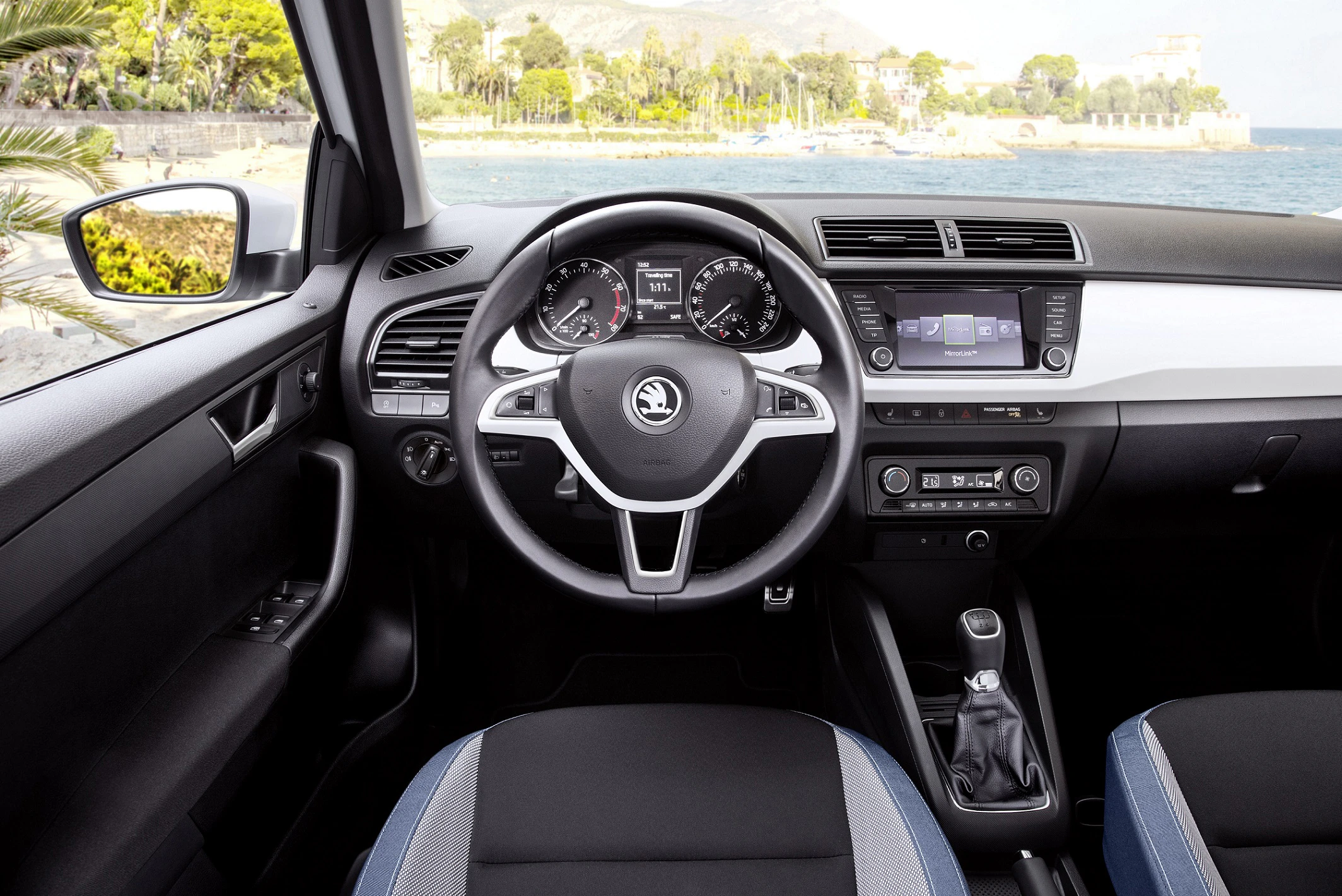 Innenraum eines Autos mit Blick auf das Lenkrad, Armaturenbrett und Schalthebel. Im Hintergrund eine Aussicht auf das Meer.