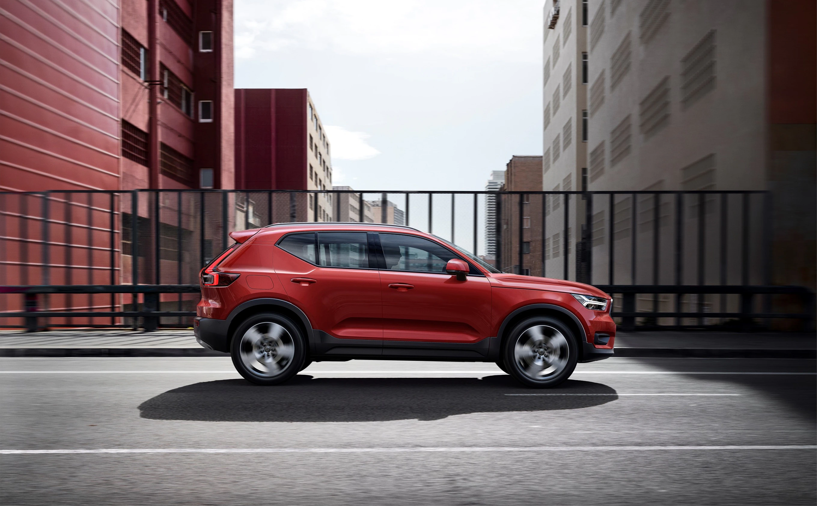 Roter SUV fährt auf städtischer Straße zwischen modernen Gebäuden. Dynamische Seitenansicht bei Tageslicht.