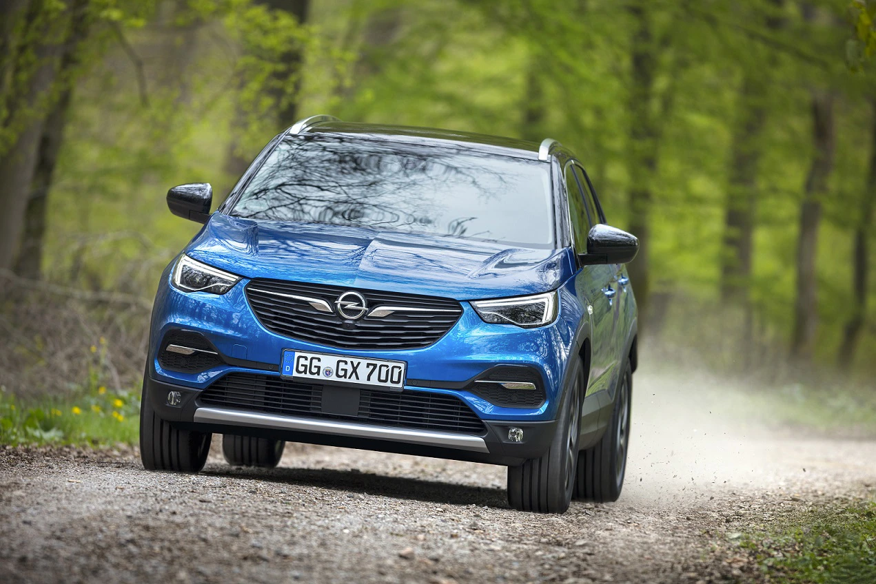 Blauer Opel SUV fährt auf einem Schotterweg durch einen grünen Wald.