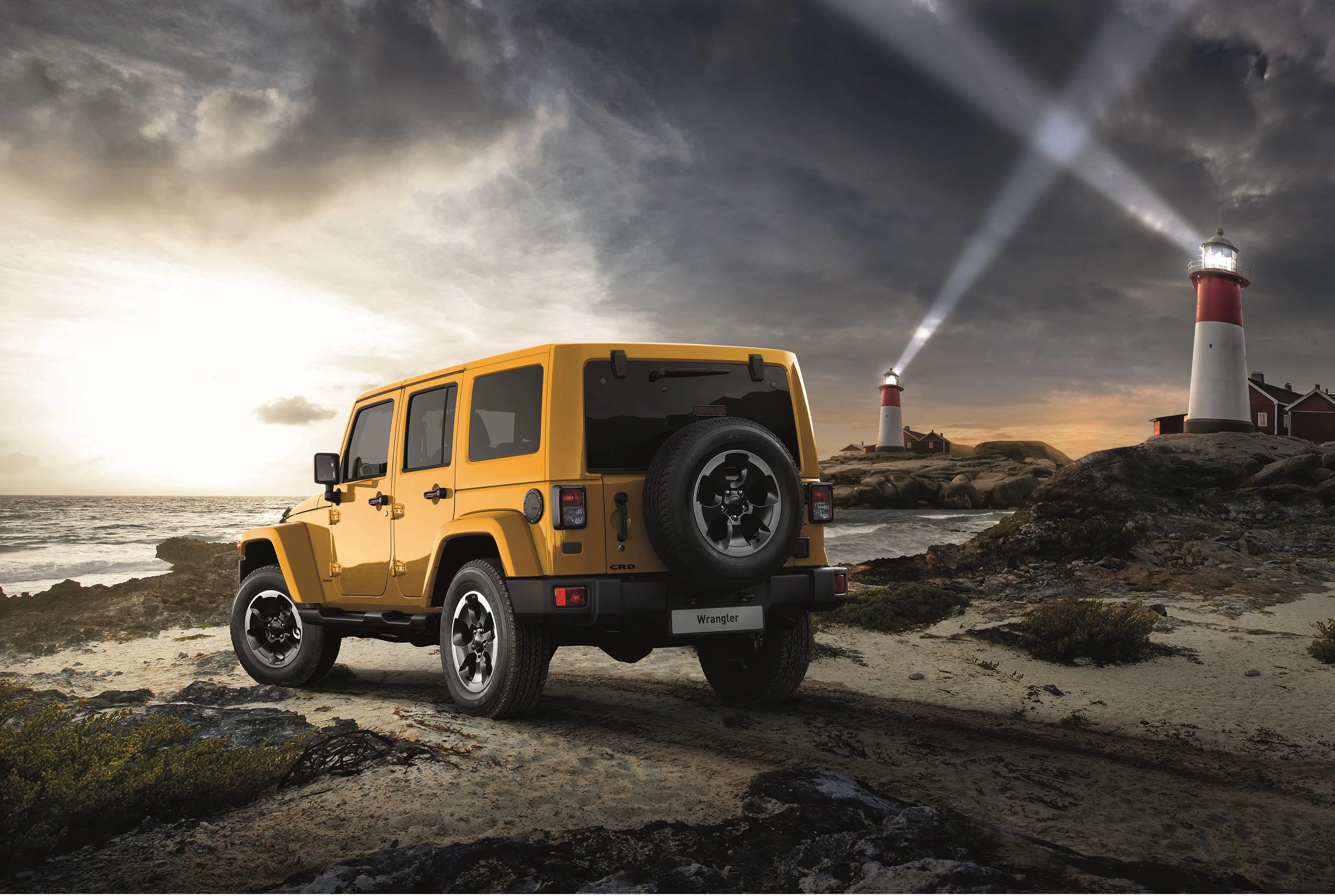 Gelber Jeep auf sandigem Pfad nahe Küste, mit zwei Leuchttürmen im Hintergrund und stürmischem Himmel.