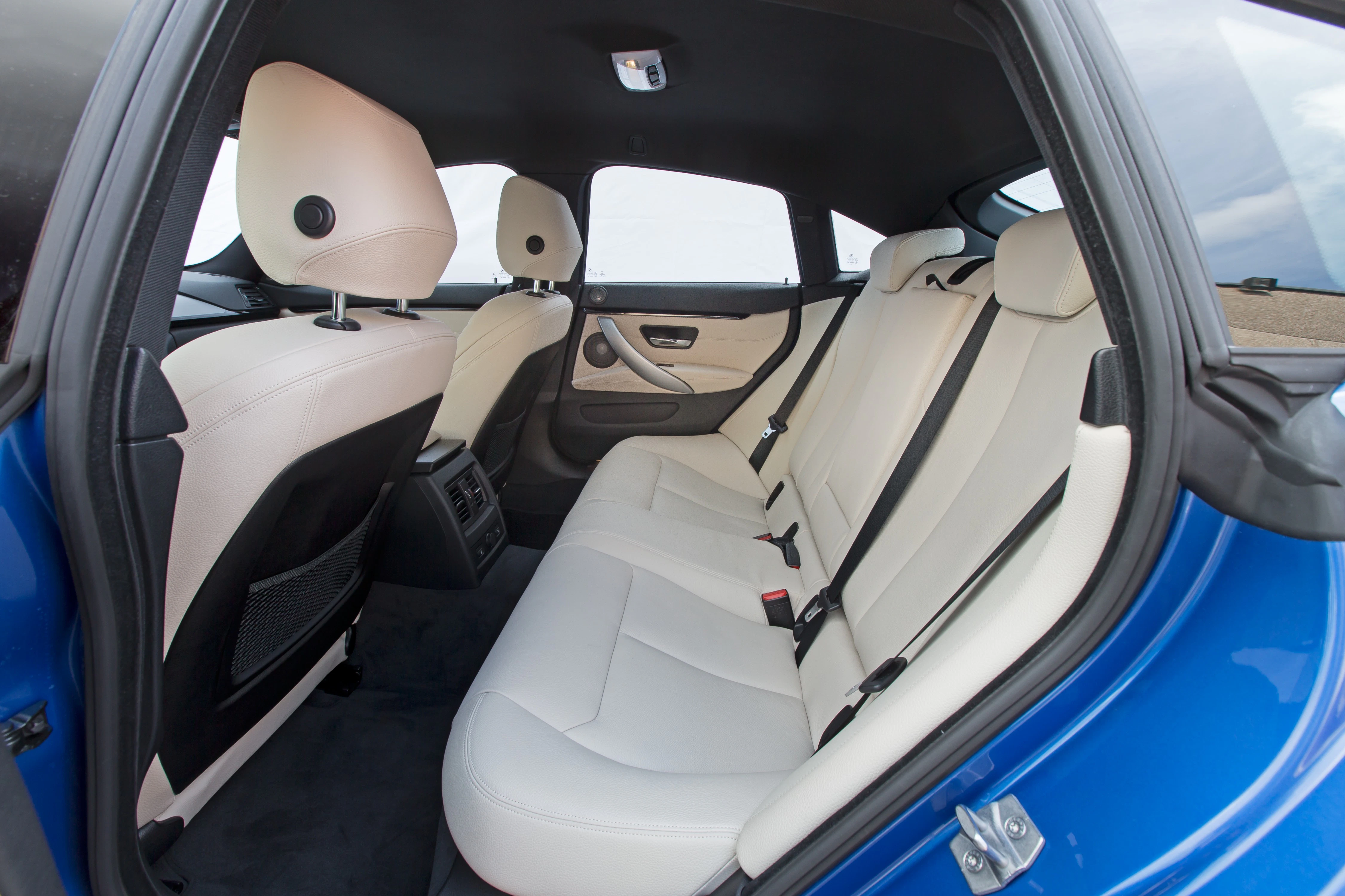 Innenansicht eines Autos mit weißen Ledersitzen und einem blauen äußeren Türrahmen, aufgenommen von der Rücksitzperspektive.