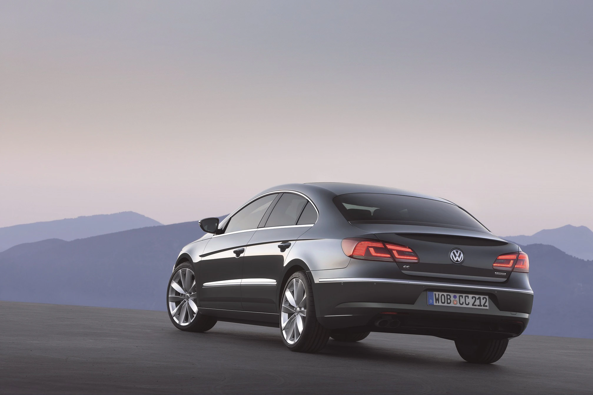 Silberner VW Passat CC, fotografiert von hinten. Im Hintergrund sind Berge und ein pastellfarbener Himmel zu sehen.
