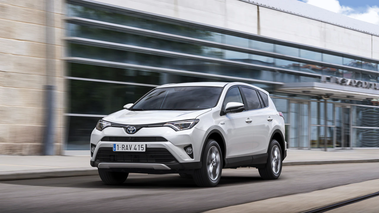 Weißer Toyota-SUV fährt auf einer Straße vor einem modernen, verglasten Gebäude.