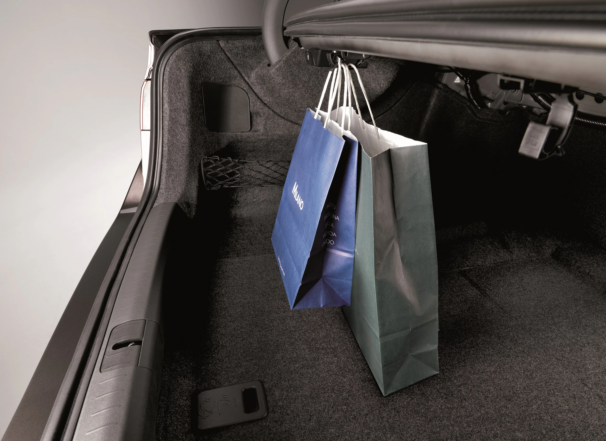 Zwei Einkaufstaschen hängen im Kofferraum eines Autos an einem Haken. Der Kofferraum ist dunkelgrau ausgekleidet.