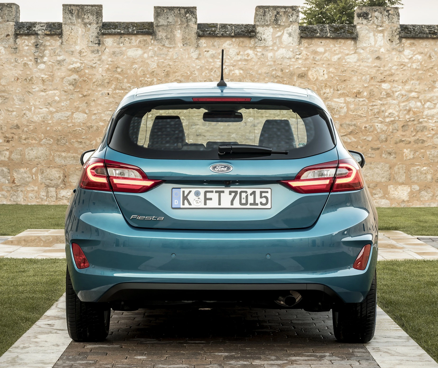 Blauer Ford Fiesta parkt vor einer Steinmauer auf gepflastertem Weg. Rückansicht zeigt Kennzeichen "K FT 7015".