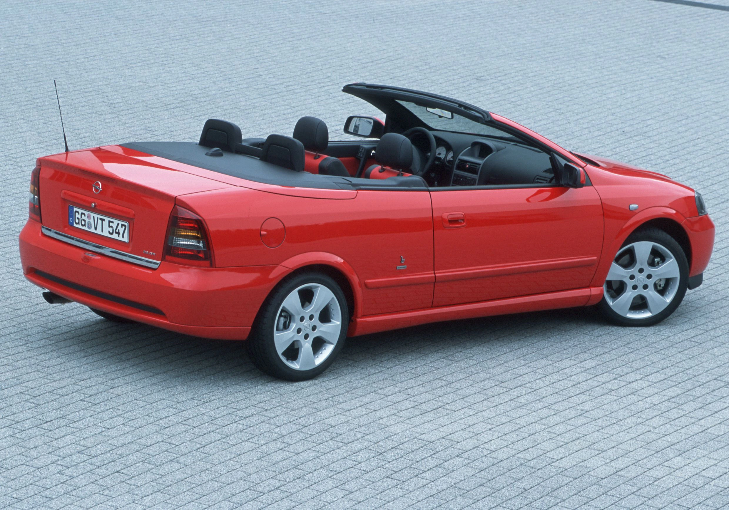 Rotes Cabriolet auf gepflastertem Untergrund, von hinten fotografiert. Auto ist offen, mit schwarzem Innenraum und glänzendem Lack.