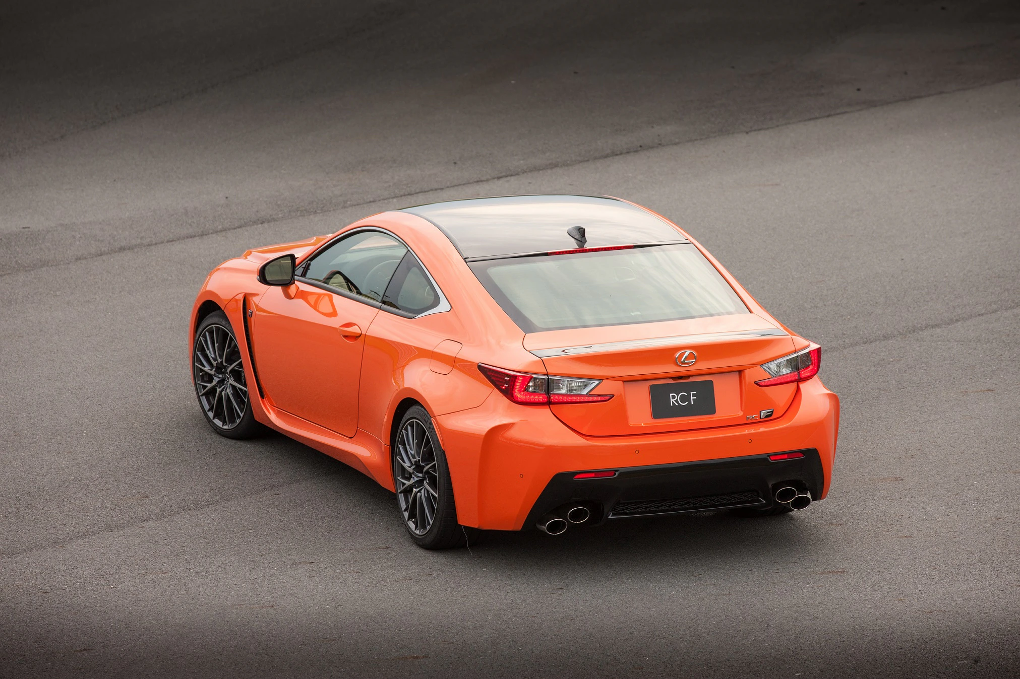 Ein oranges Sportcoupé, von hinten fotografiert, steht auf einer grauen Straße. Es hat markante Rückleuchten und vier Auspuffrohre.