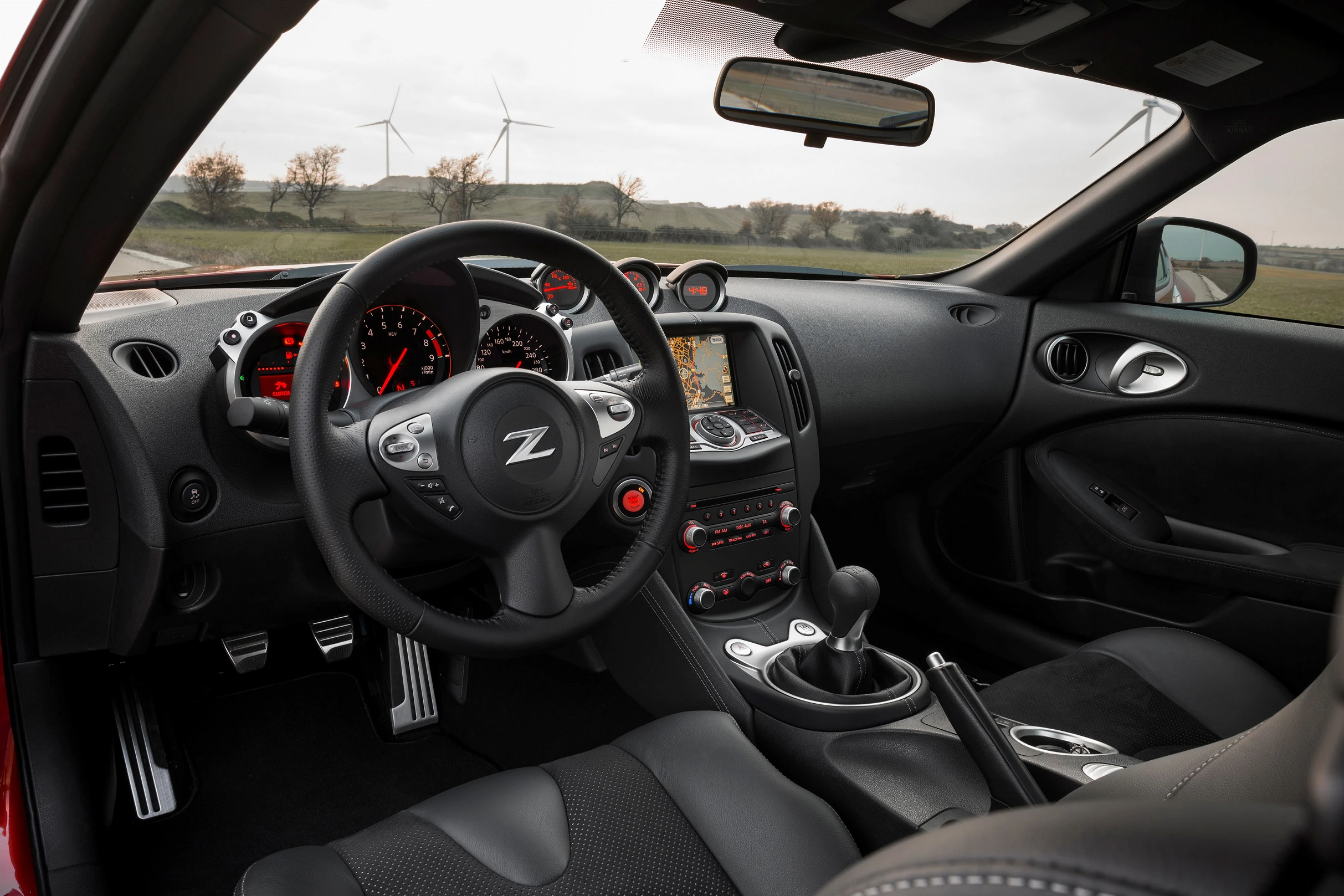 Innenraum eines Sportwagens mit Z-förmig markiertem Lenkrad, Tachometer, Schaltgetriebe und einem Display auf dem Armaturenbrett.