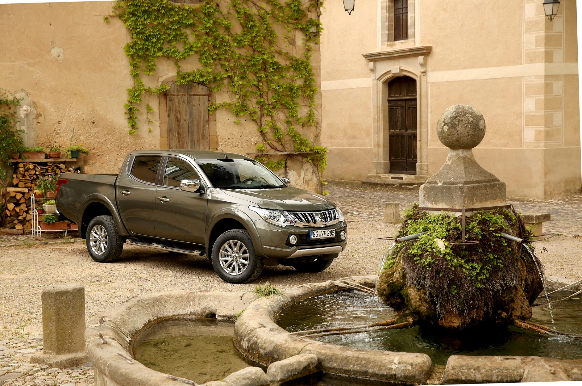 Brauner Pick-up-Truck neben einem alten Brunnen in einem historischen Innenhof mit Kletterpflanzen an den Wänden.