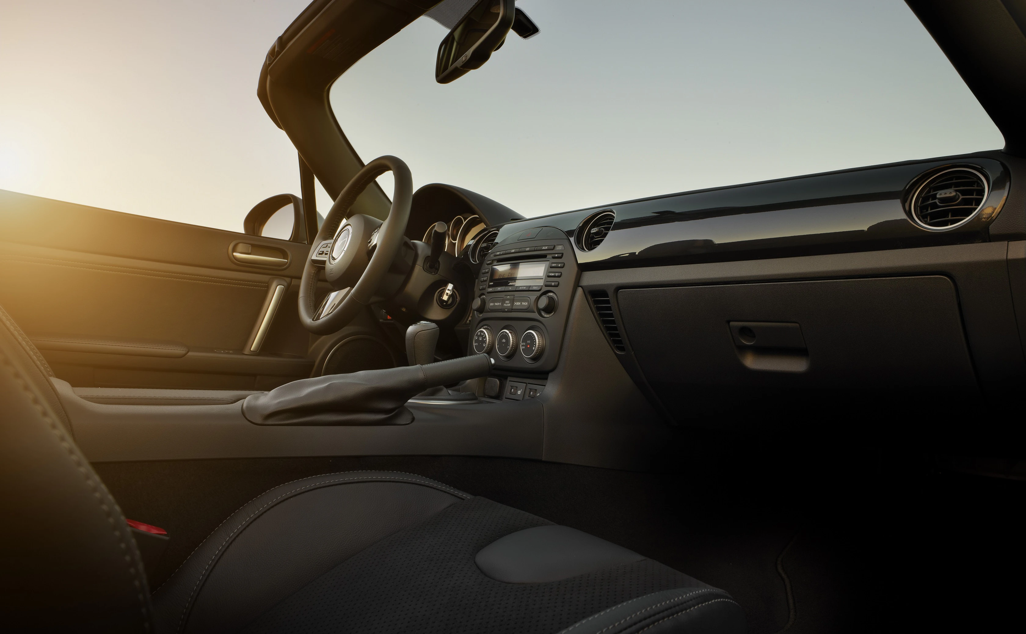 Innenraum eines neuen Cabrio-Sportwagens bei Sonnenuntergang, mit elegantem Armaturenbrett und modernem Lenkrad, ohne sichtbare Personen.