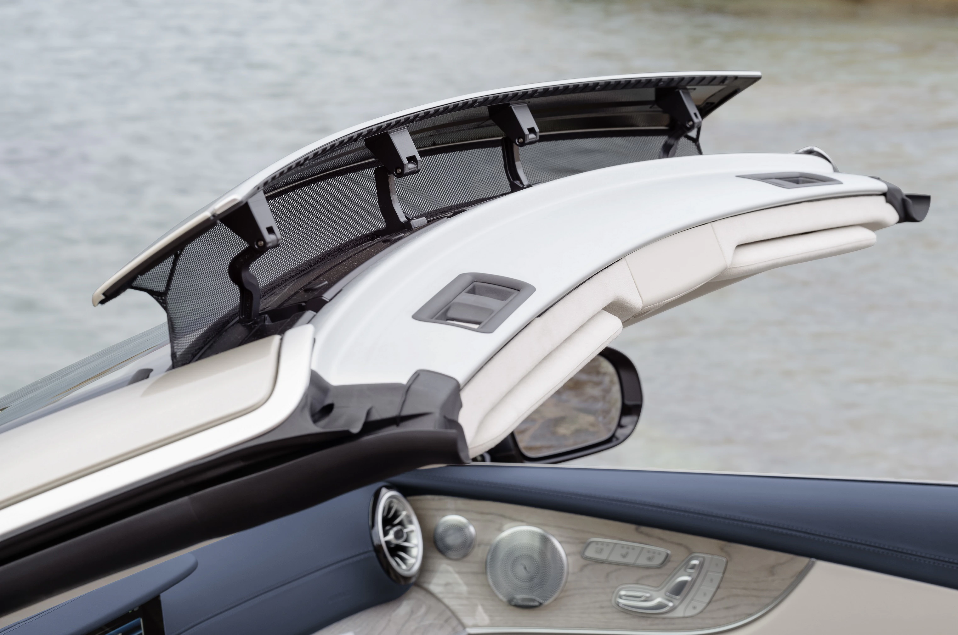 Nahaufnahme eines geöffneten Cabriolet-Dachs eines Luxusautos am Wasser, zeigt Innenraum-Details und stilvolle Verkleidungselemente.