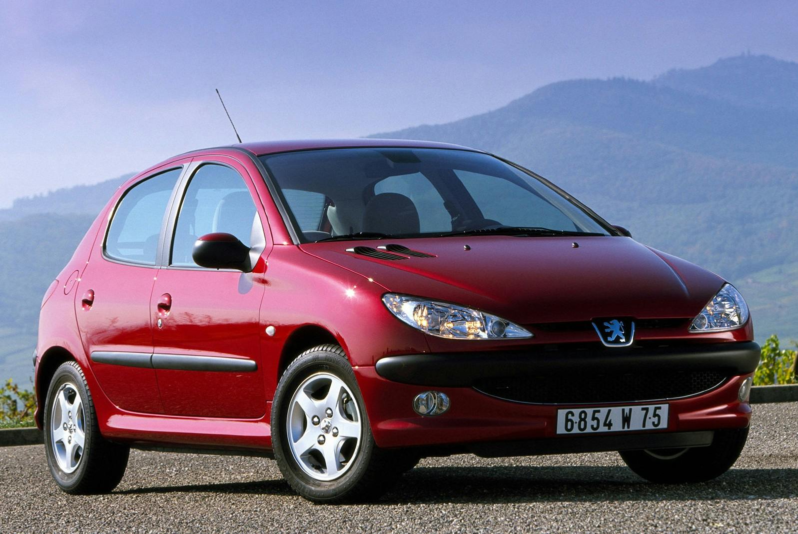 Roter Peugeot 206 parkt vor einer bergigen Landschaft mit klarem Himmel im Hintergrund.