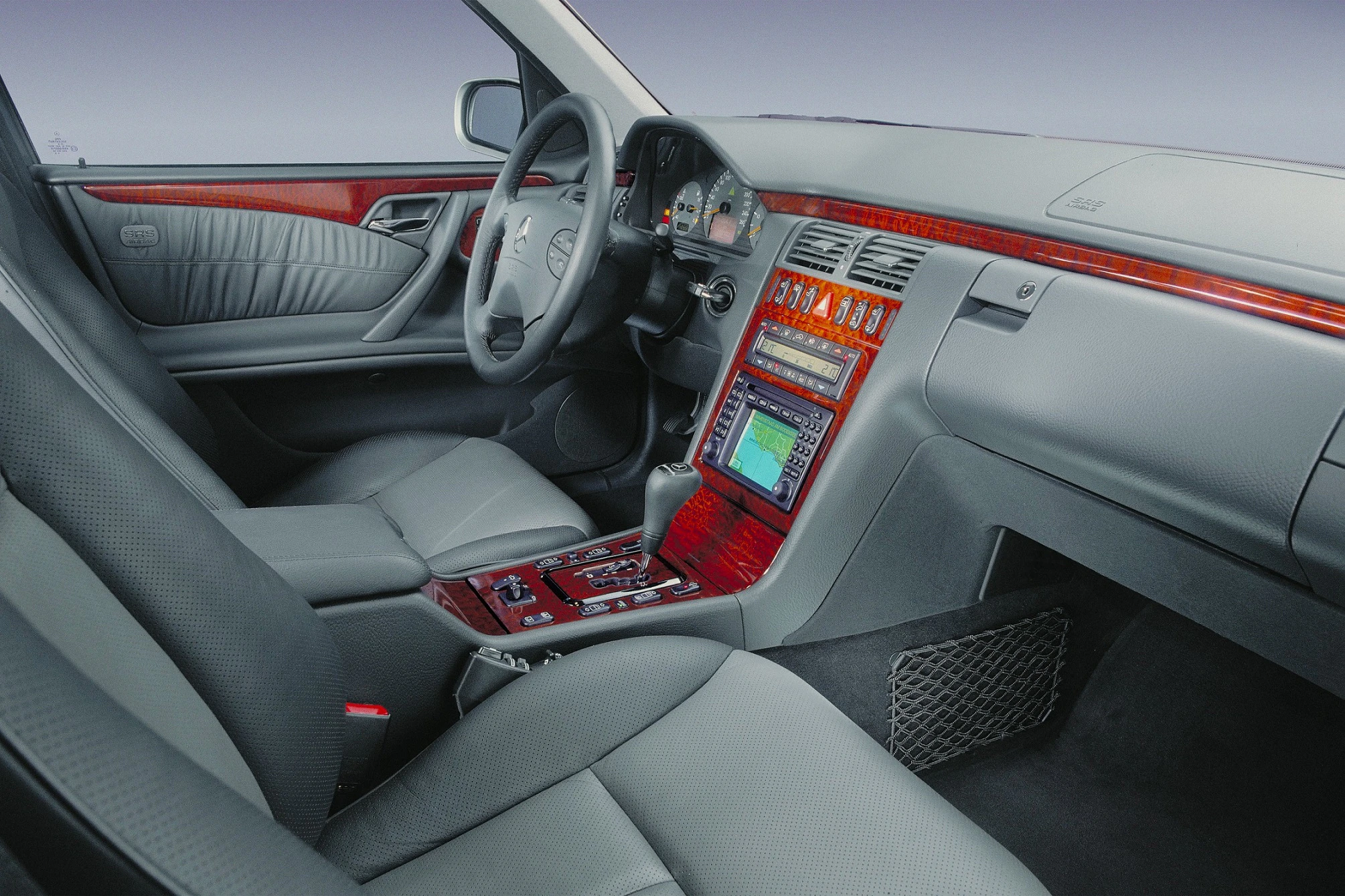 Innenraum eines Autos mit grauen Ledersitzen, Holzverkleidung am Armaturenbrett und Lenkrad, eingebautes Navigationssystem.