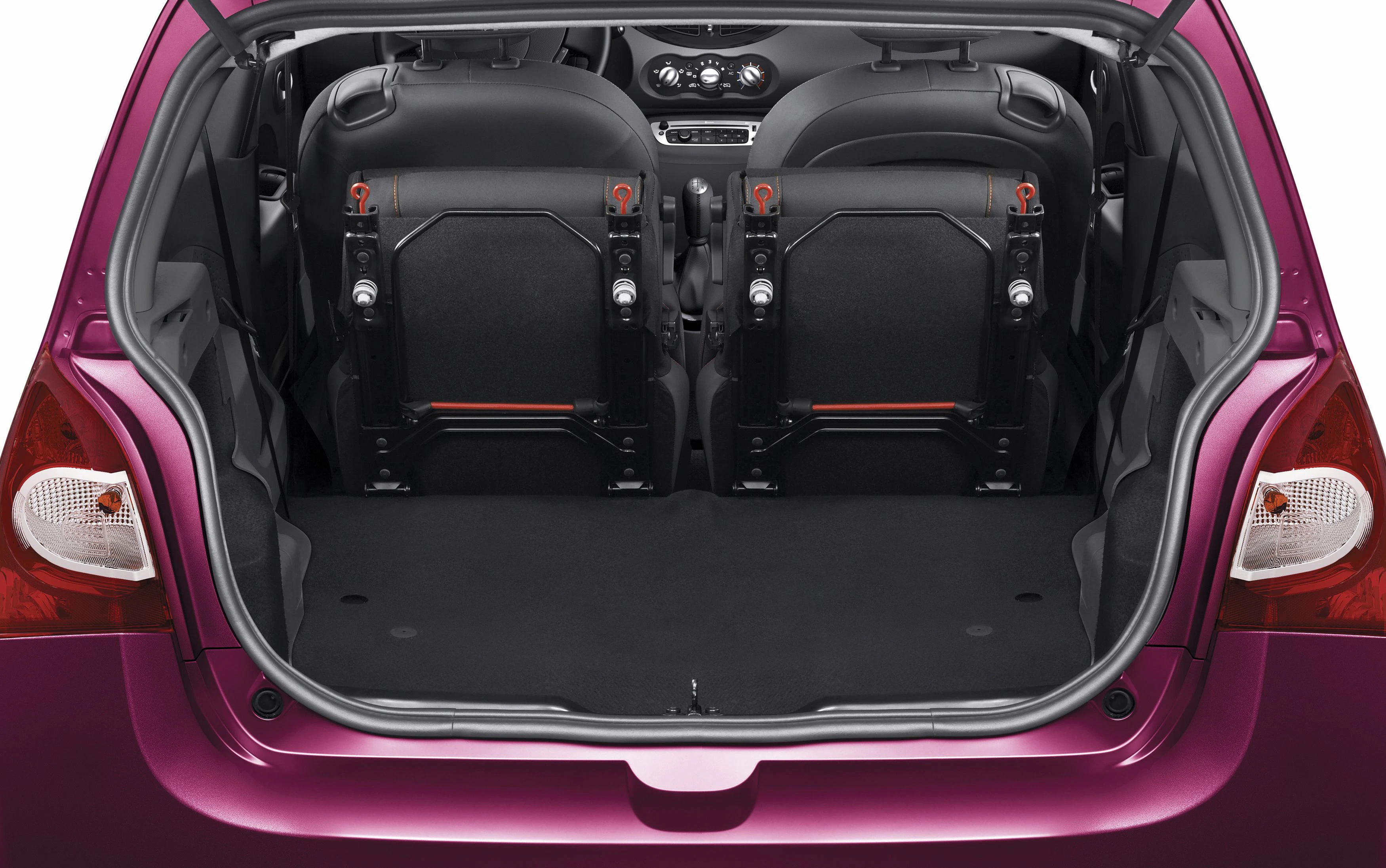 Kofferraum eines pinken Autos mit umgeklappten Rücksitzen, die nach vorne gerichtet sind. Großer, leerer Stauraum sichtbar.